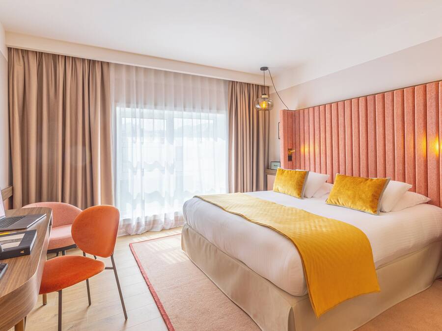 Ein Hotelzimmer mit einem großen Bett, einem Schreibtisch mit einem Laptop, einem Sessel und einem Fernseher.