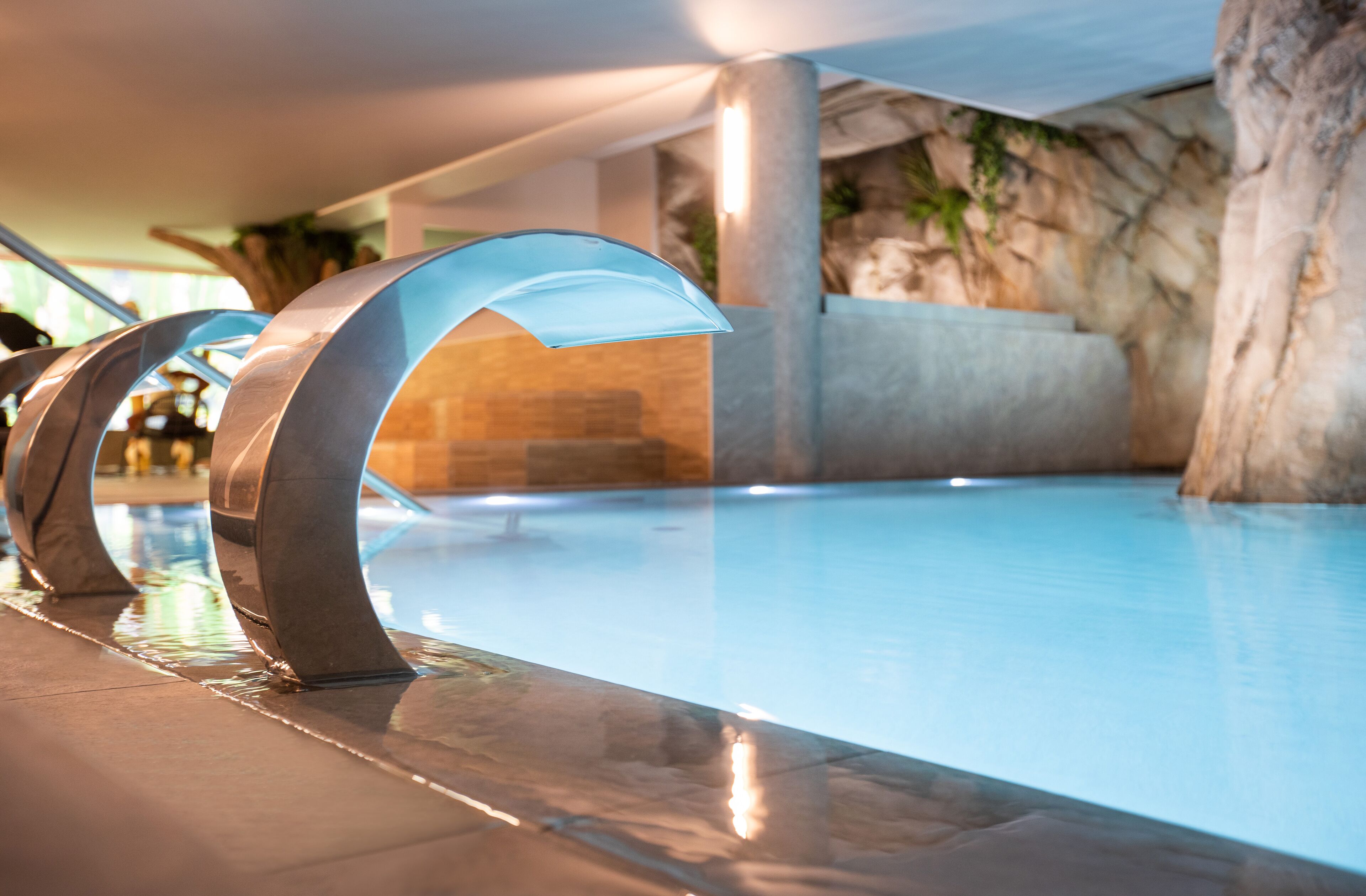 Ein moderner Innenpool mit klarem Wasser, umgeben von Steinwänden und einem Metallgeländer.