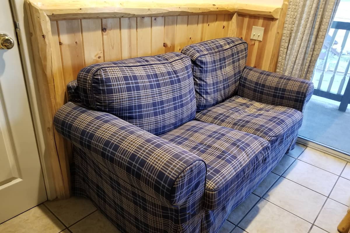 Ein blau-kariertes Sofa in einem Raum mit Holzwandverkleidung und Fliesenboden.