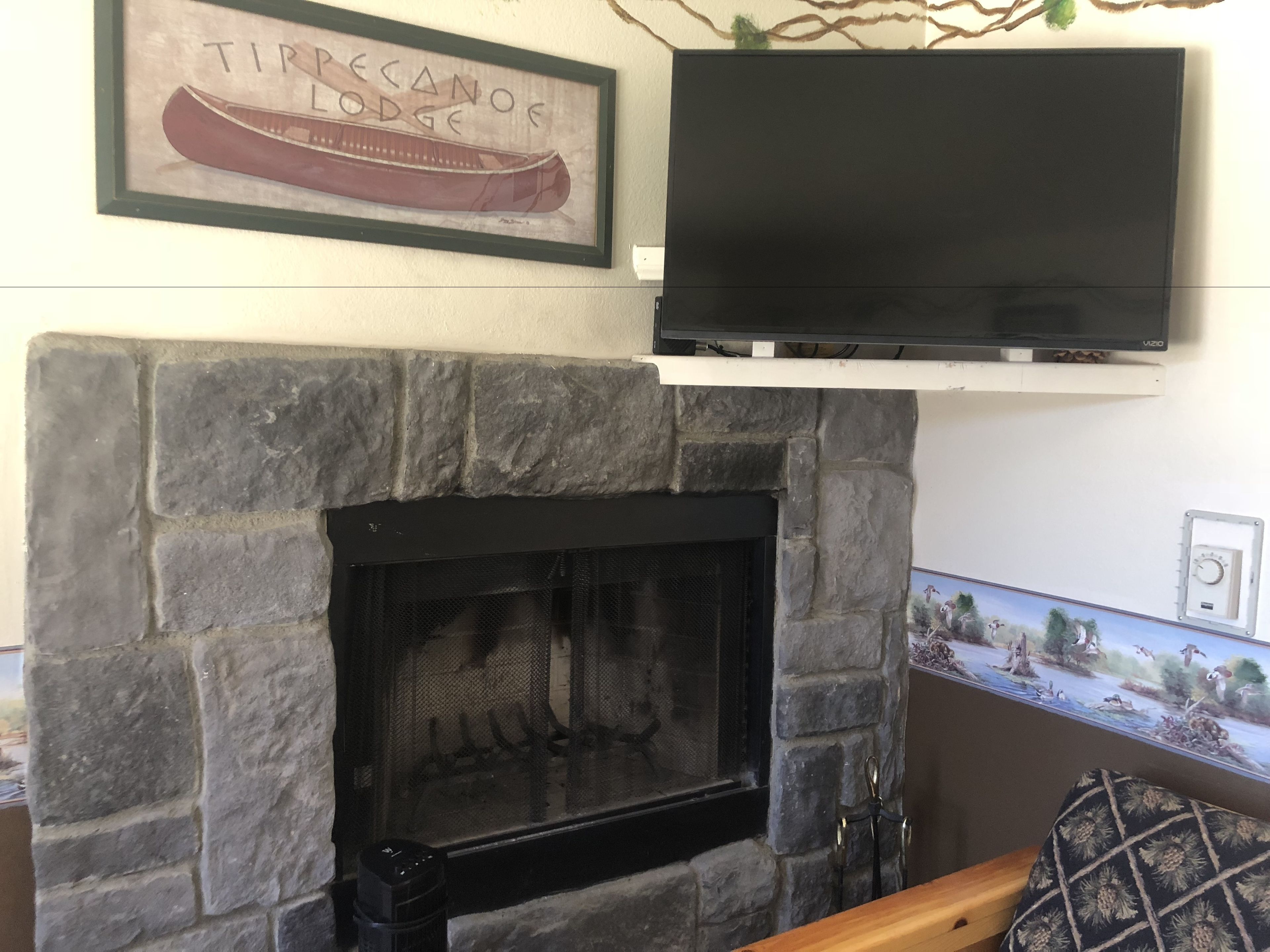 A stone fireplace with a TV above it, a framed picture of a canoe, and a decorative wall piece.