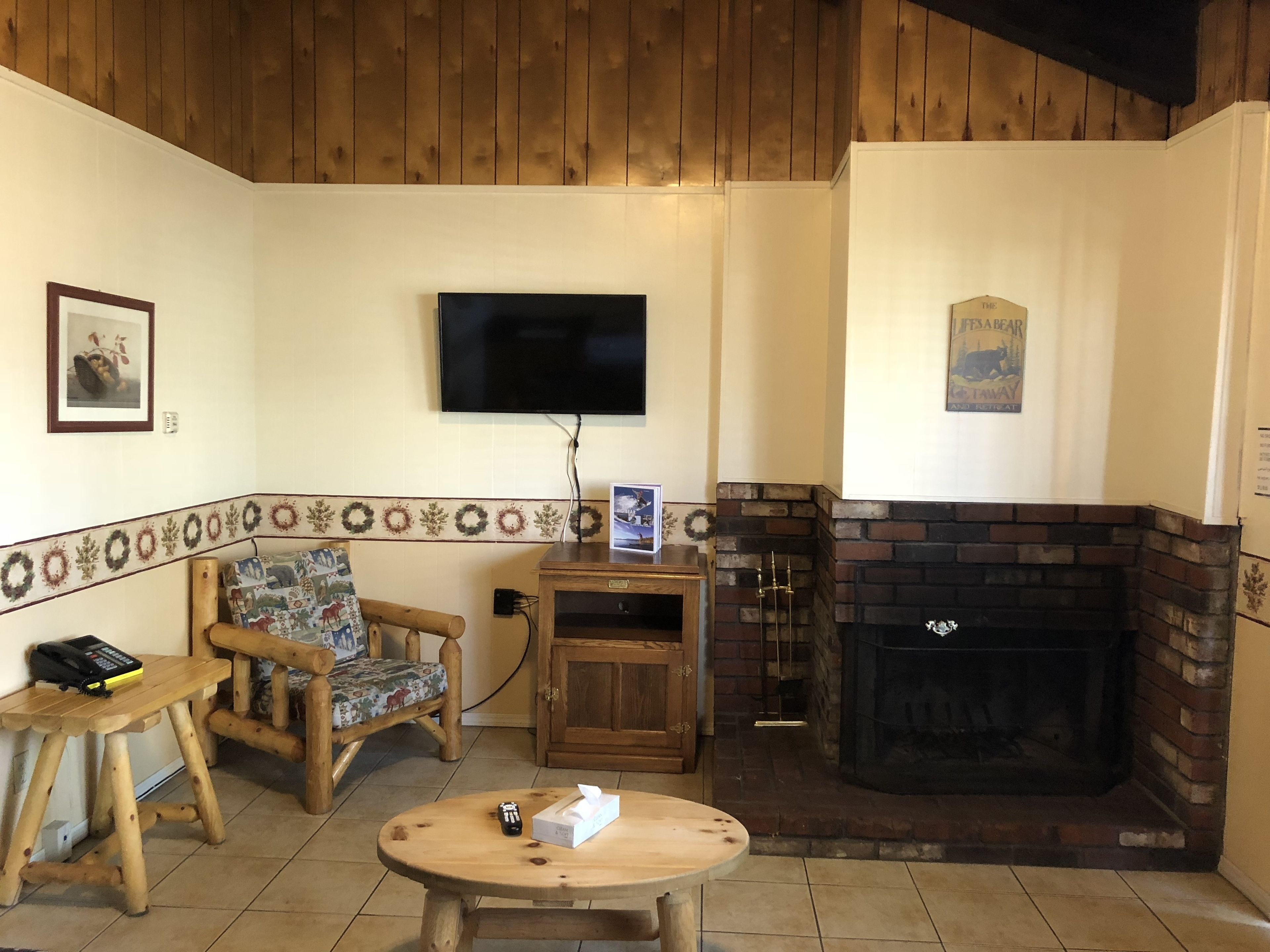 A cozy living room with a fireplace, wooden furniture, a flat-screen TV, and a decorative border.