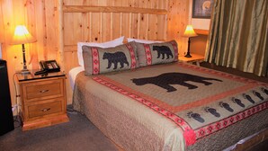 A wooden-paneled room with a bed, two bedside lamps, a telephone, and a nightstand. - Fireside Lodge (Big Bear Lake)