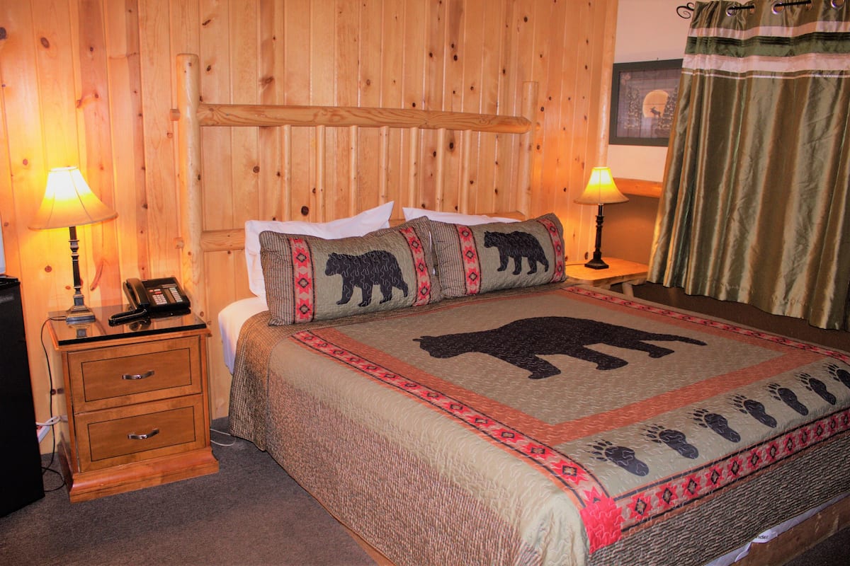 Ein Zimmer mit Holzwänden, einem Bett, zwei Nachttischlampen, einem Telefon und einem Nachttisch.