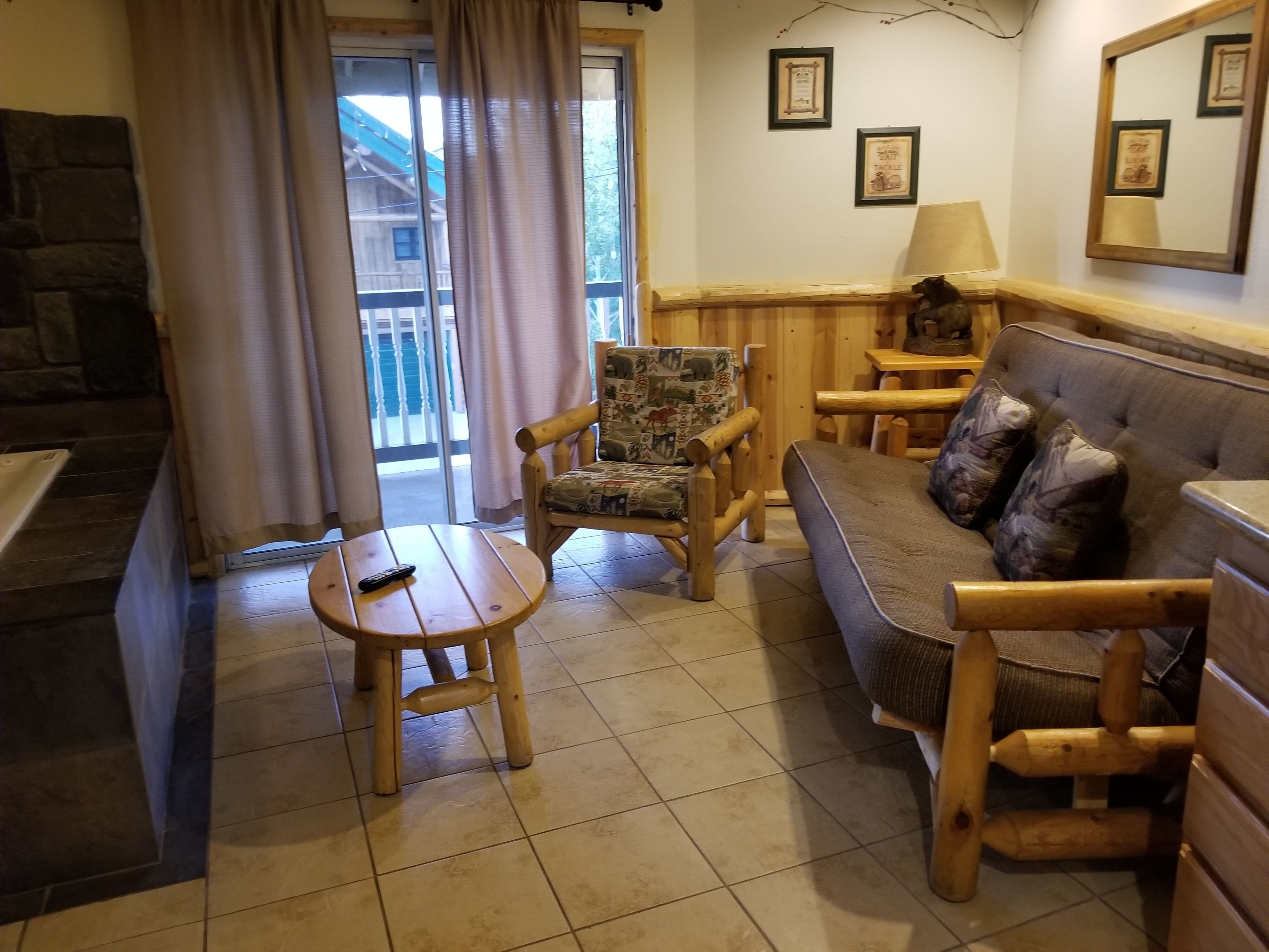 Una sala acogedora con un sofá de madera, un sillón estampado y una pequeña mesa de madera.
