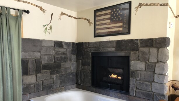A stone-walled bathroom with a large bathtub, a fireplace, and a framed American flag. - Fireside Lodge (Big Bear Lake)