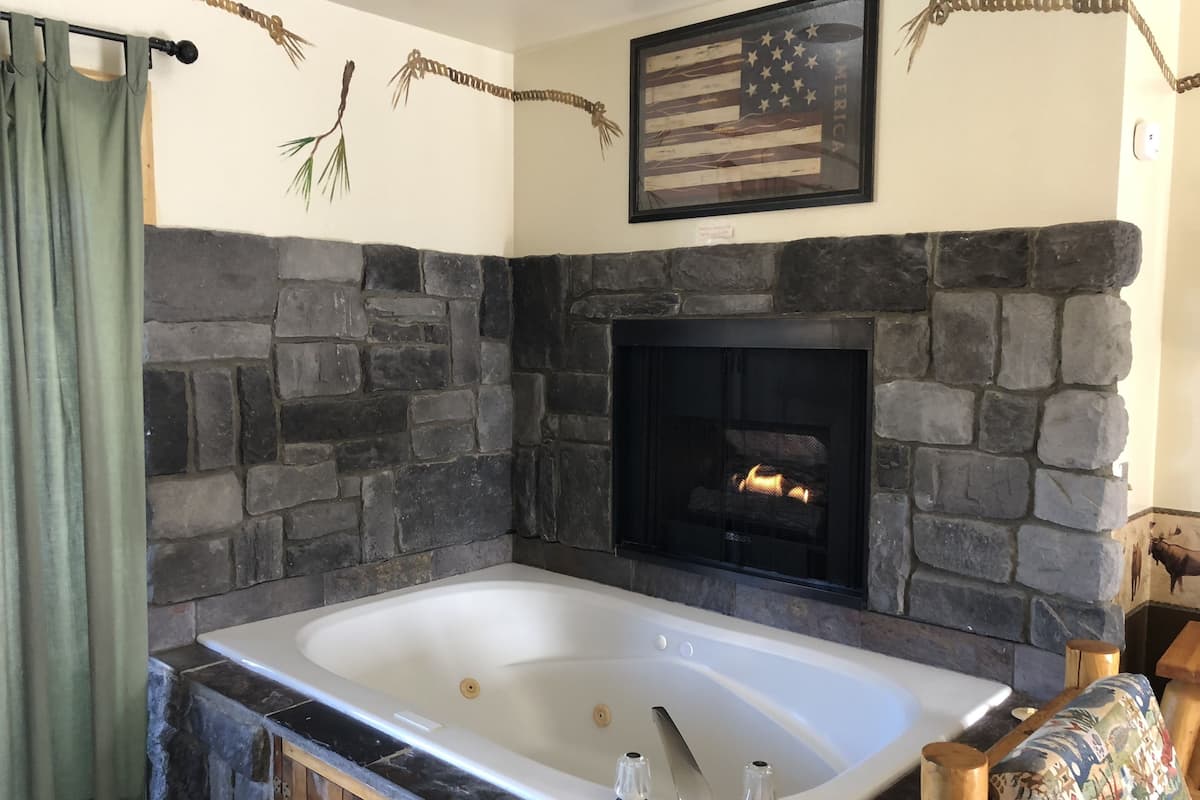 Ein Badezimmer mit Steinwänden, einer großen Badewanne, einem Kamin und einer gerahmten amerikanischen Flagge.