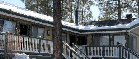 A cabin with a snow-covered roof, a wooden deck, and a staircase leading to the entrance.