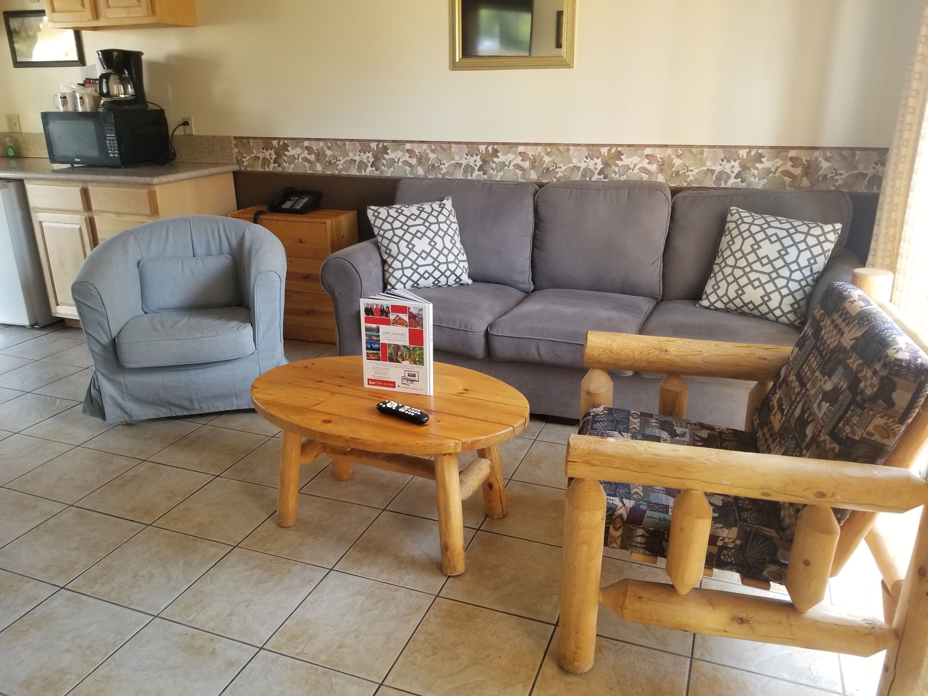 A living room with a grey sofa, a wooden coffee table, a grey armchair, and a small wooden side table with a phone.