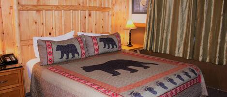 Habitación con paneles de madera, una cama con edredón con estampado de oso, una lámpara de noche y un teléfono sobre una mesita de noche de madera.