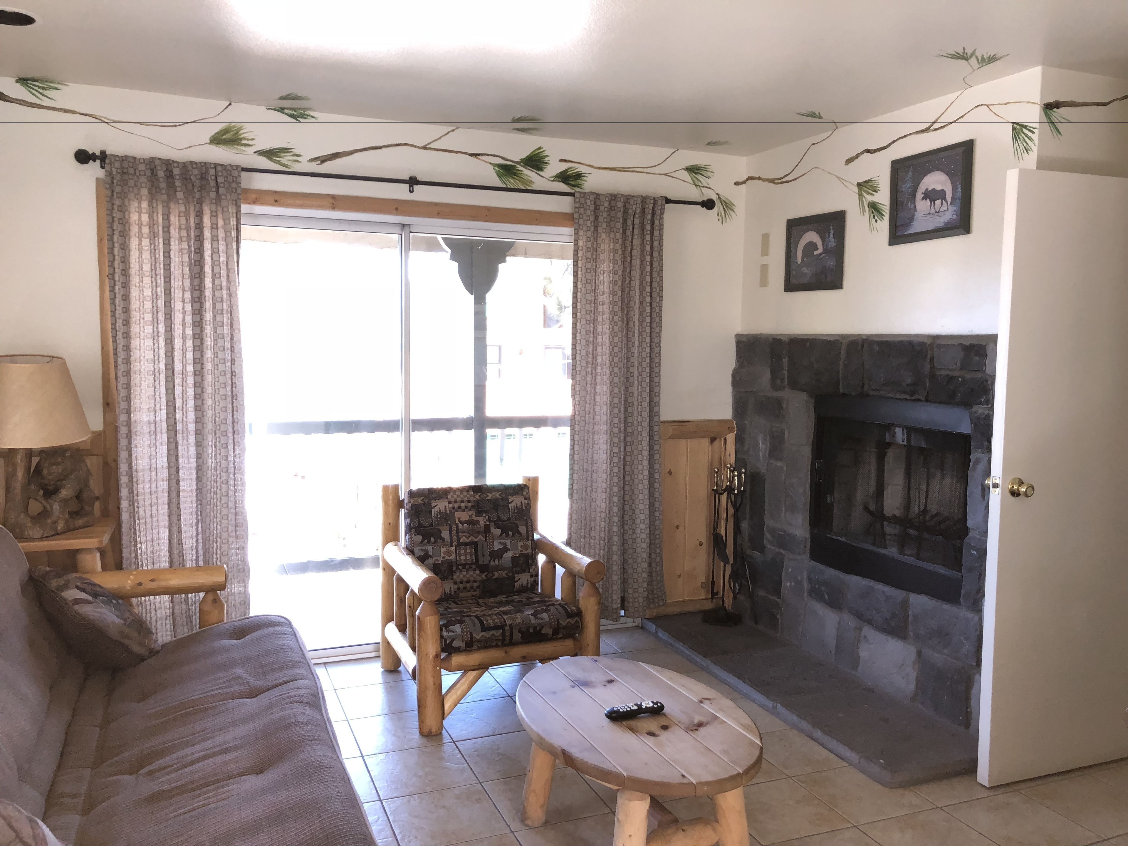 A living room with a sofa, a patterned armchair, a wooden coffee table, a fireplace, and a door leading to an outdoor area.
