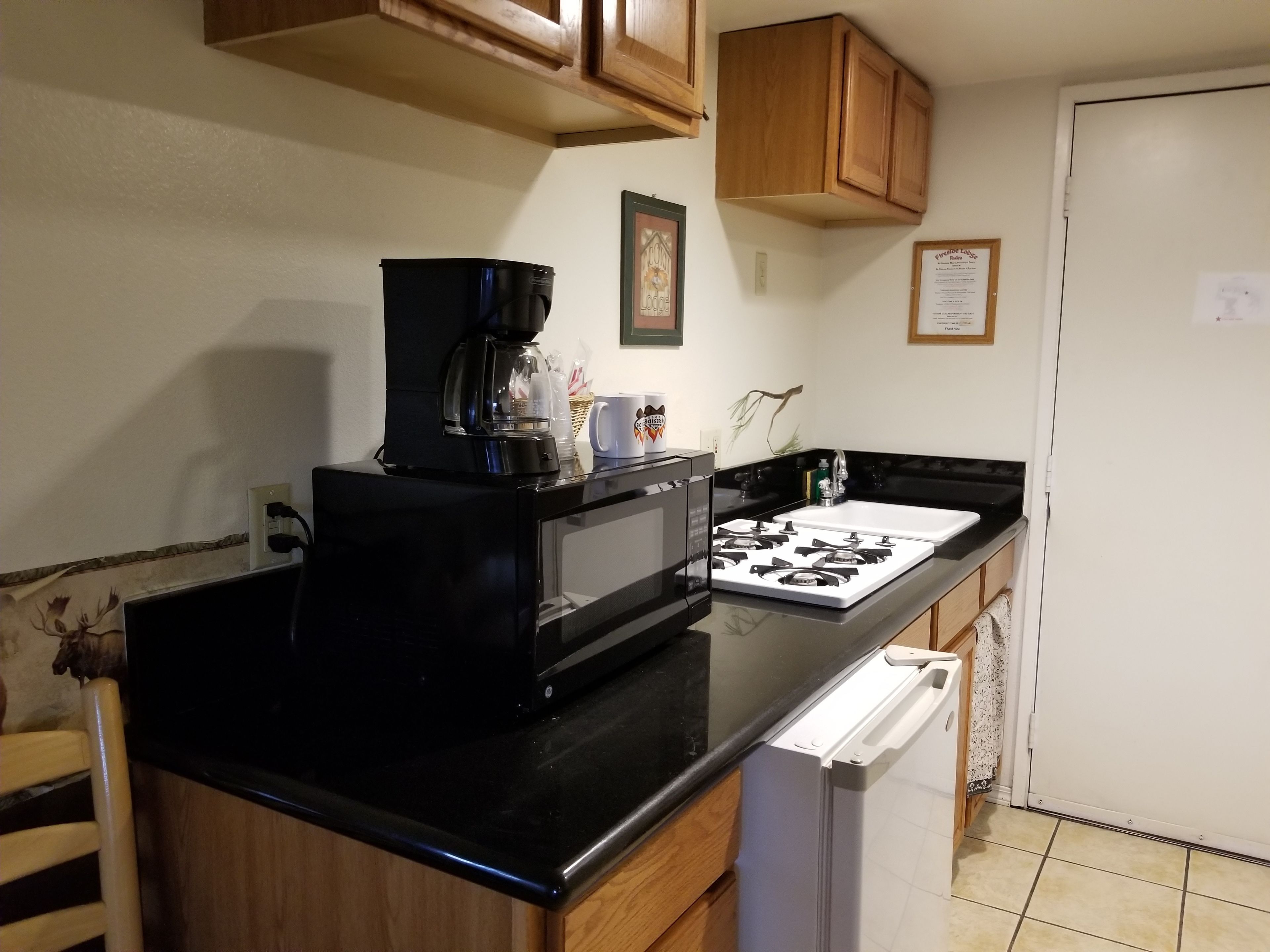 A compact kitchen with a black microwave, a coffee maker, a stove, and wooden cabinets.
