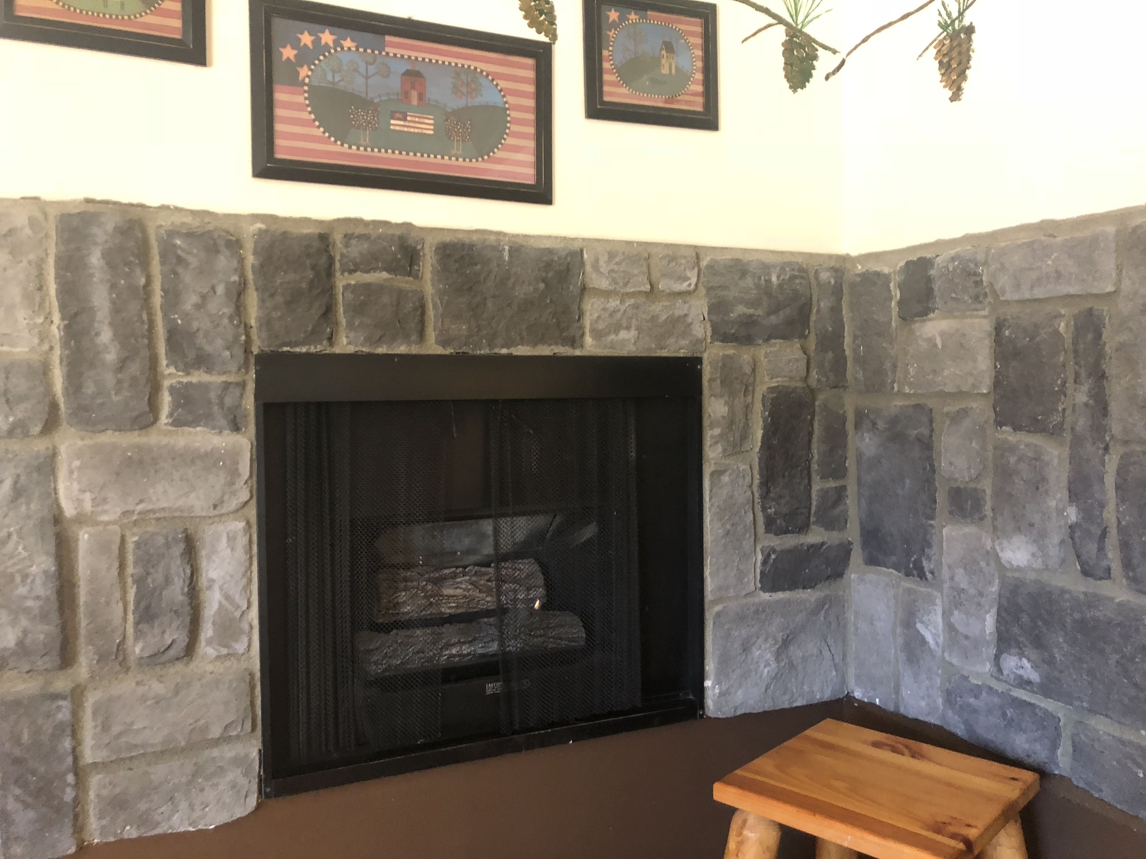 A stone fireplace with a black screen, a wooden bench, and framed pictures on the wall.