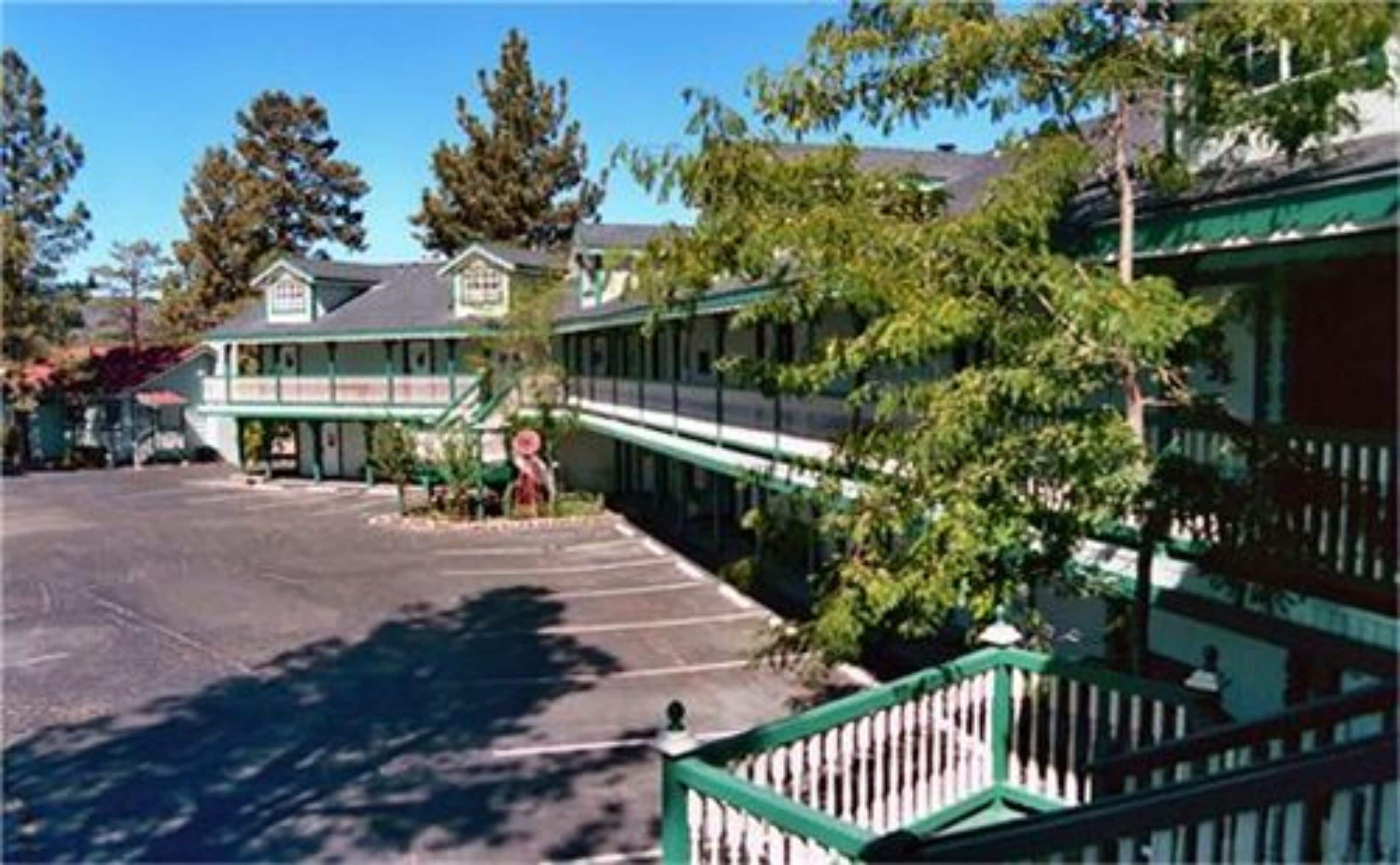 A motel with a covered parking area, a green railing, and trees in the background.