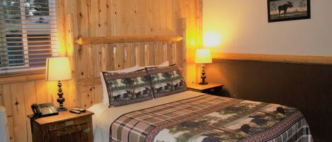 Una habitación con paneles de madera, una cama, dos lámparas de noche, una mesita con un teléfono y un cuadro en la pared.
