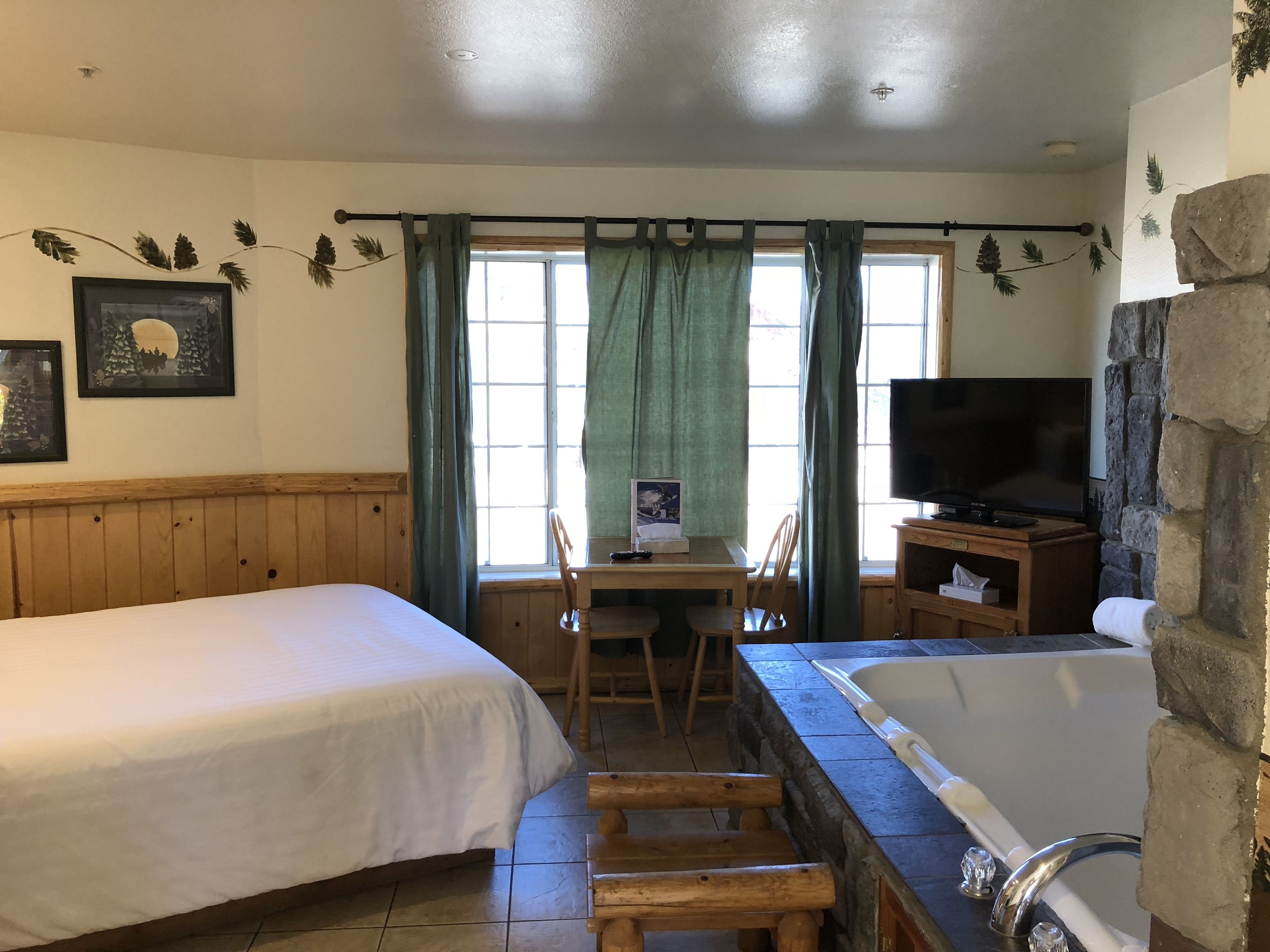 A room with a bed, a desk with a chair, a television, and a bathtub.