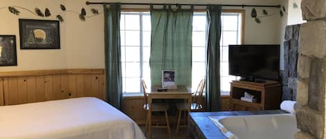 A room with a bed, a desk with a chair, a television, and a bathtub.