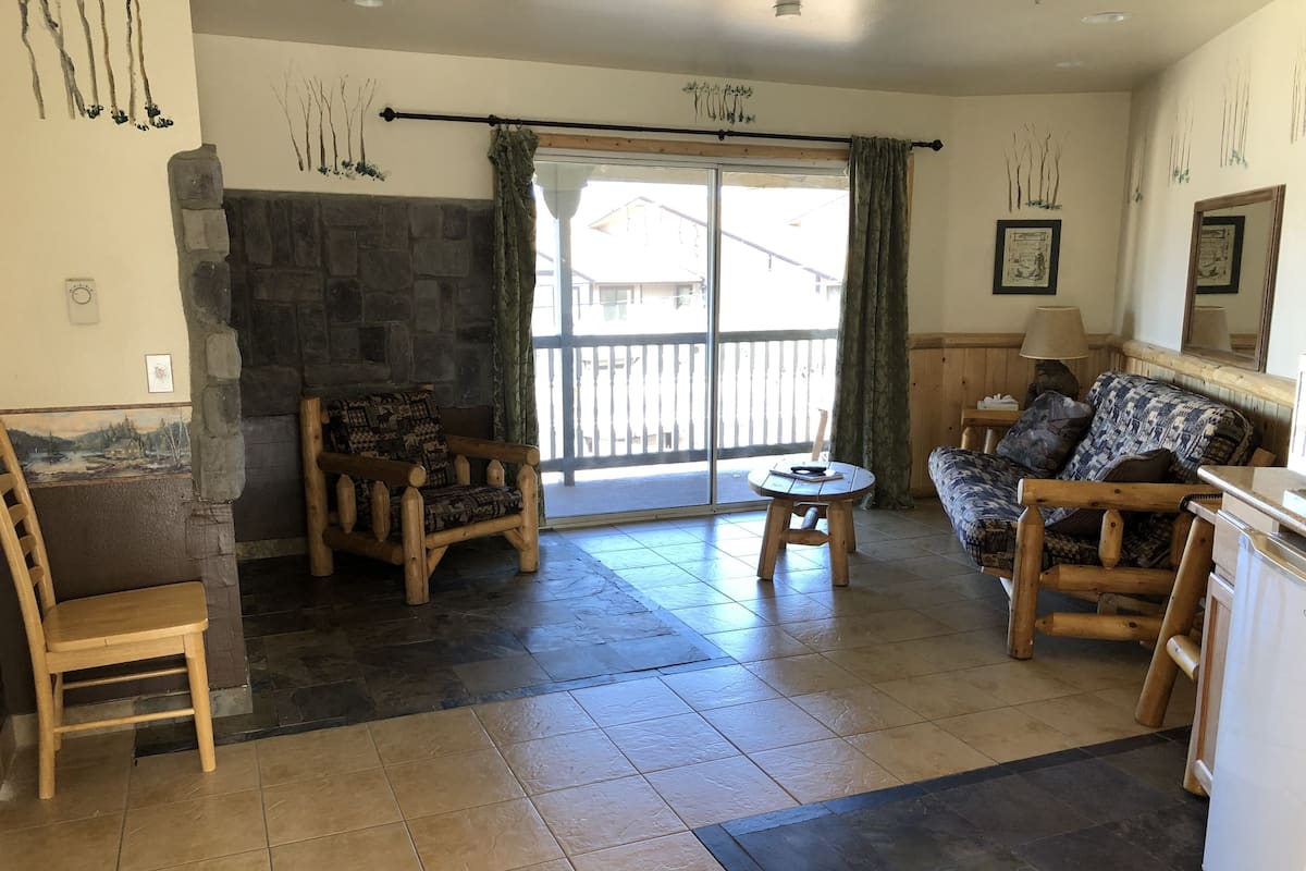 Ein gemütliches Wohnzimmer mit Kamin aus Stein, Holzmöbeln und Blick durch eine große Schiebetür.