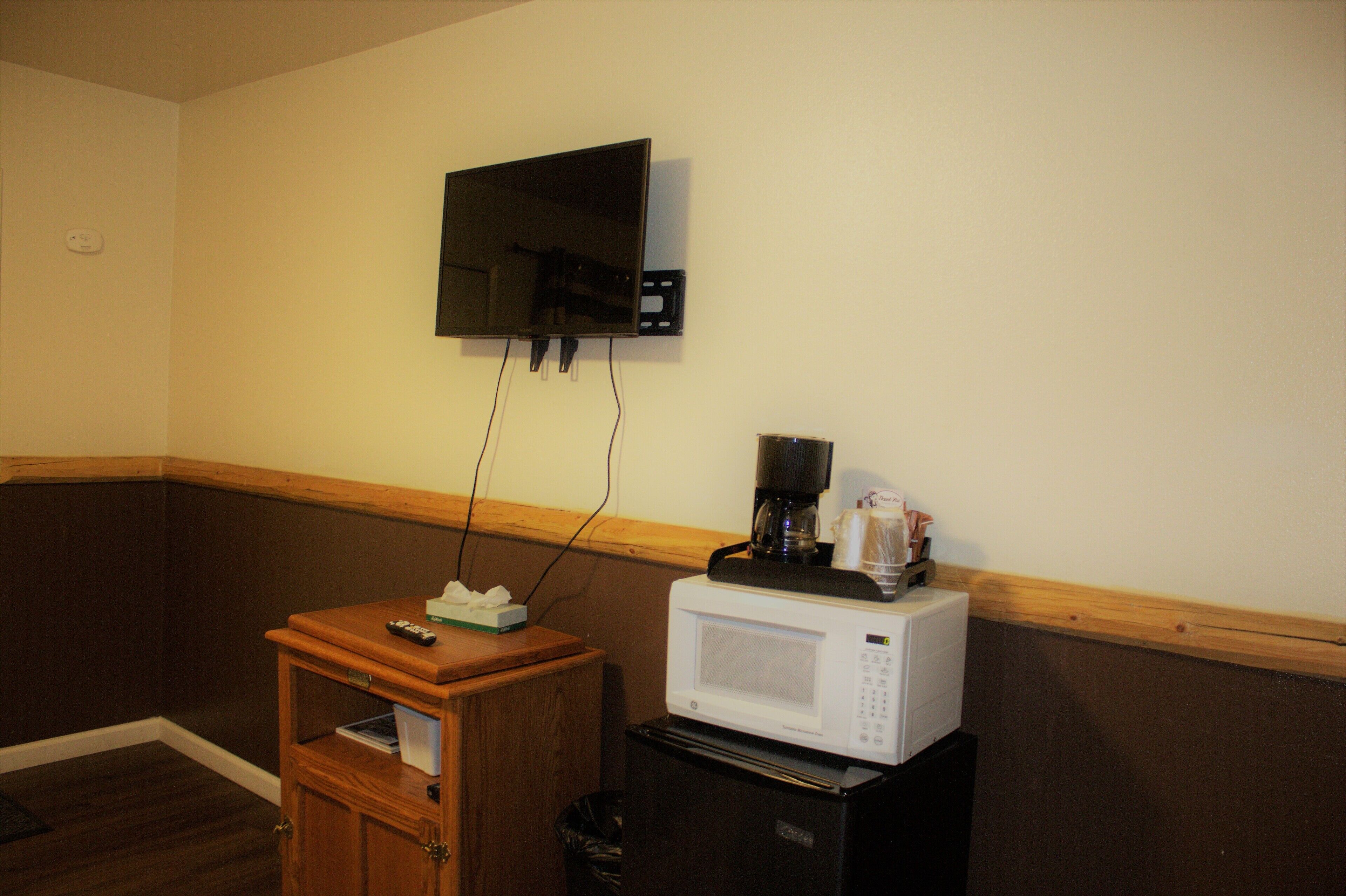 Una kitchenette con microondas, cafetera y televisor montado en la pared.