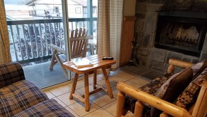 A cozy living room with a sofa, a wooden chair, a small table, and a fireplace. - Fireside Lodge (Big Bear Lake)