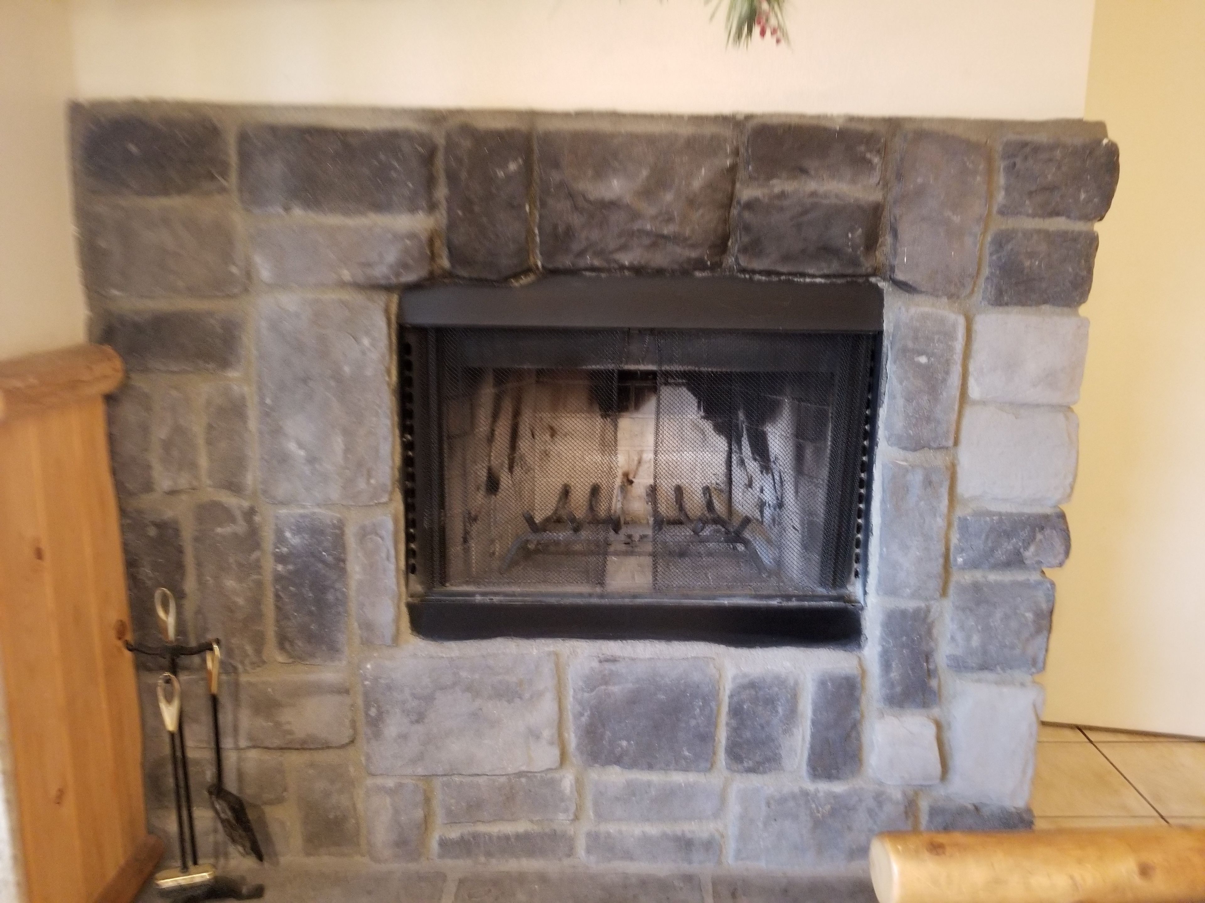 Una chimenea de piedra con una protección metálica, un banco de madera y un soporte metálico con un gancho.