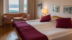 A hotel room with a bed, two chairs, a desk, a lamp, and two paintings on the wall. - 2Home Stockholm South (Arsta)