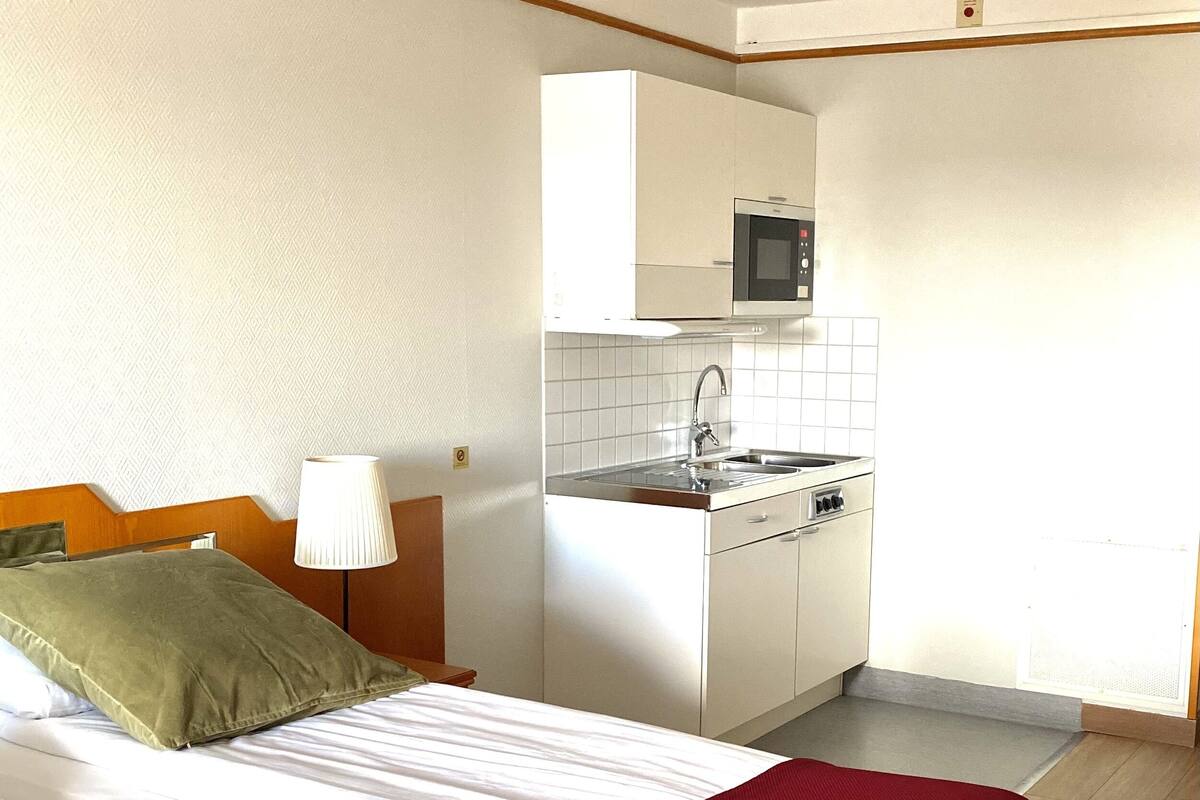 A hotel room with a bed, a kitchenette, and a wooden floor.
