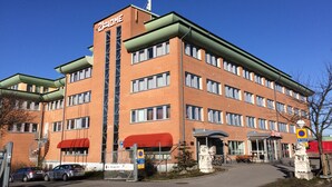 A multi-story building with a prominent '2-HOME' sign, a gated entrance, and a parking area with cars. - 2Home Stockholm South (Arsta)