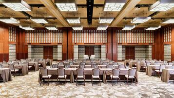 Un amplio salón de conferencias con varias mesas y sillas, techo alto con iluminación empotrada y una alfombra estampada.