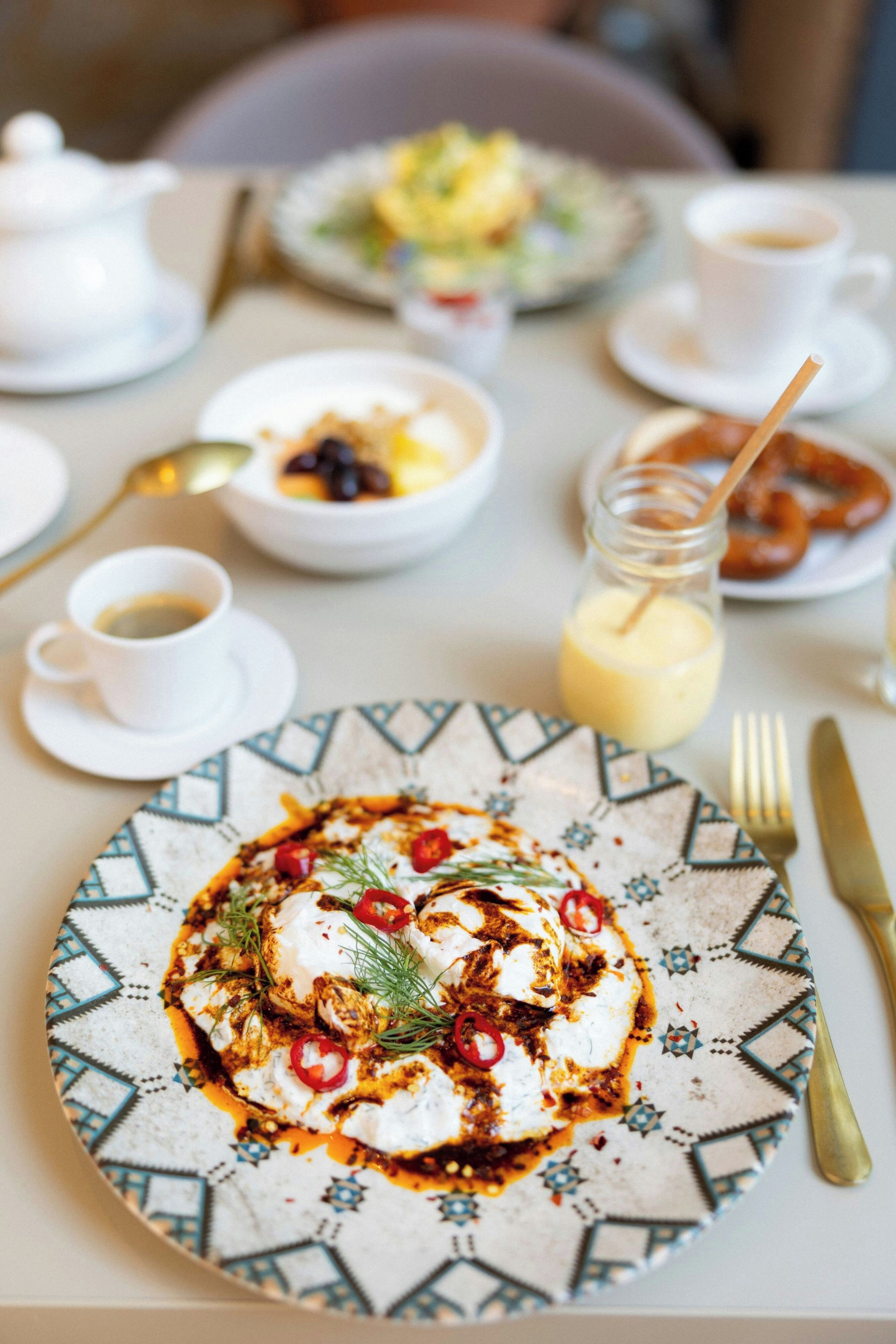 A dining table with a plate of food, a cup of coffee, and a glass of drink.
