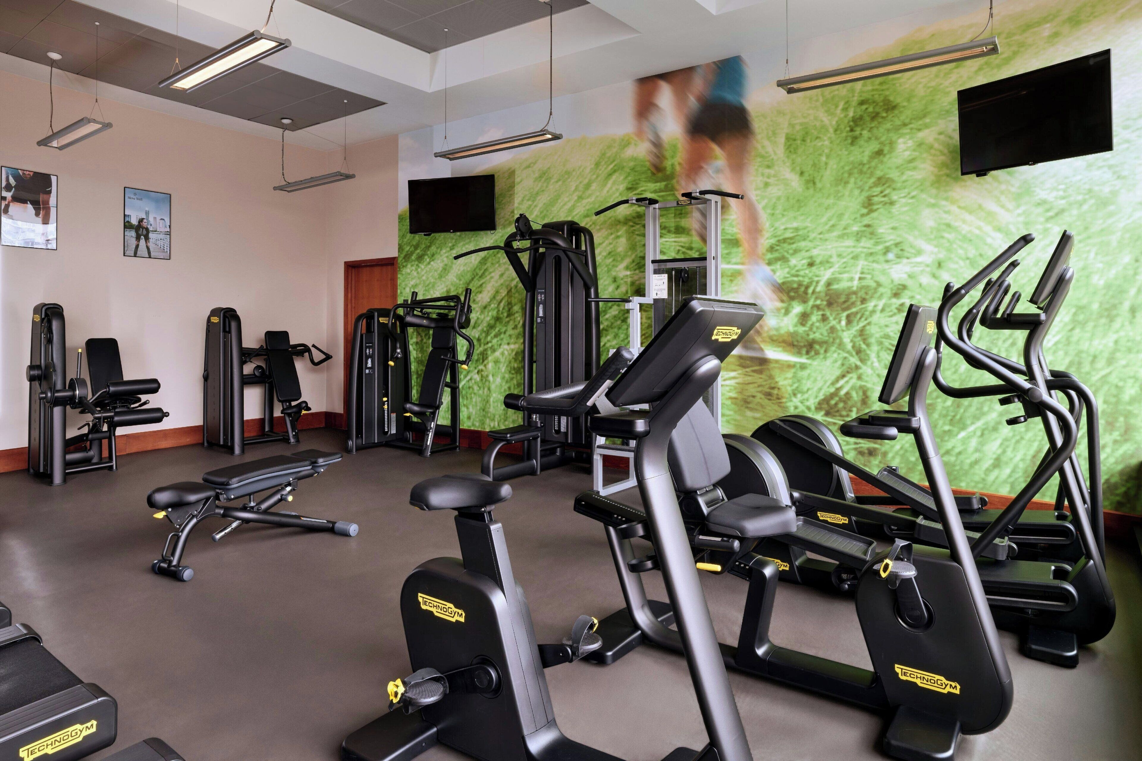 Ein Fitnessstudio mit unterschiedlichen Trainingsgeräten, darunter Laufbänder, Ergometer und Kraftgeräte.