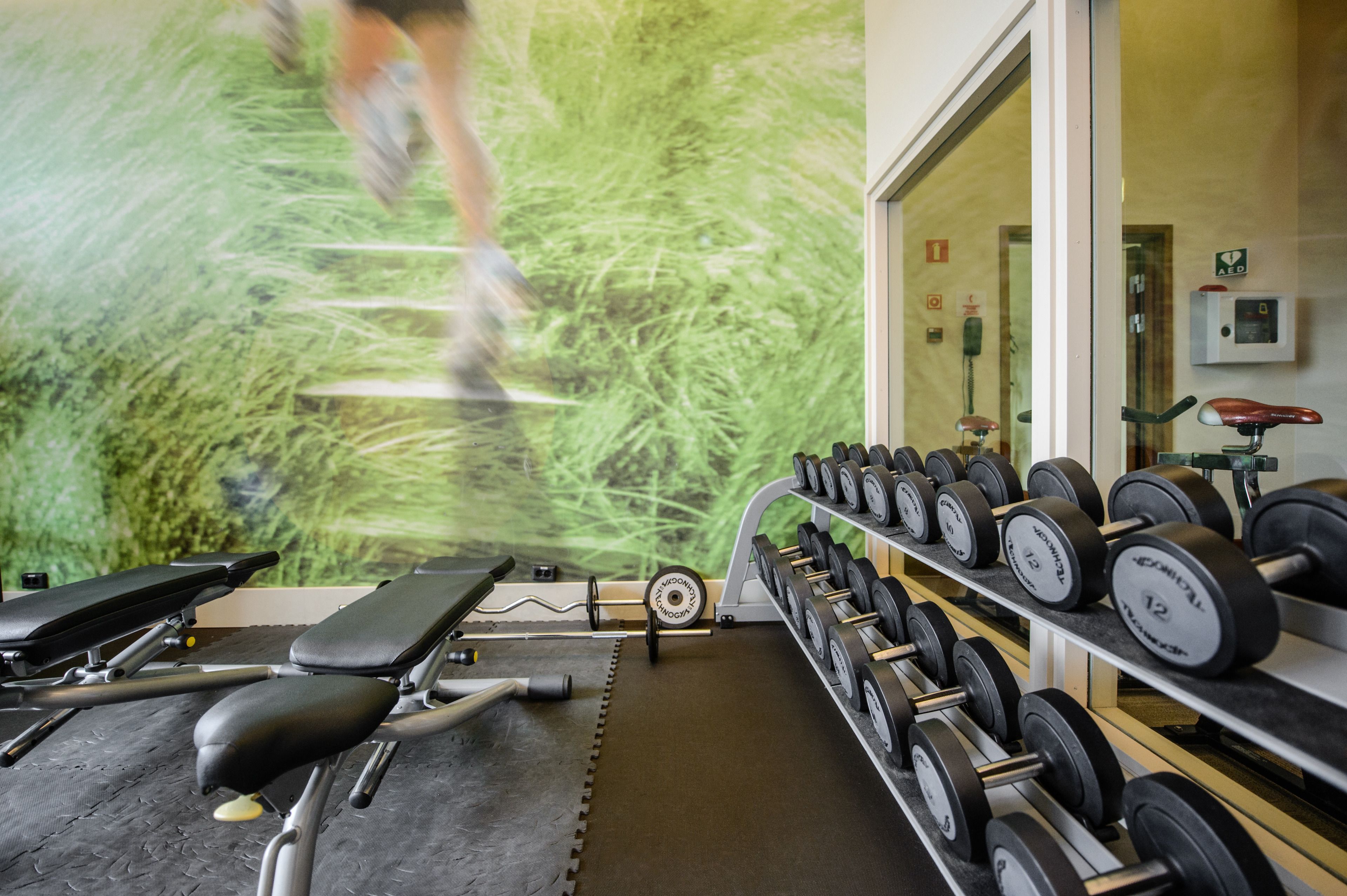 A gym with exercise equipment, including dumbbells and benches, and a wall mural of a runner.