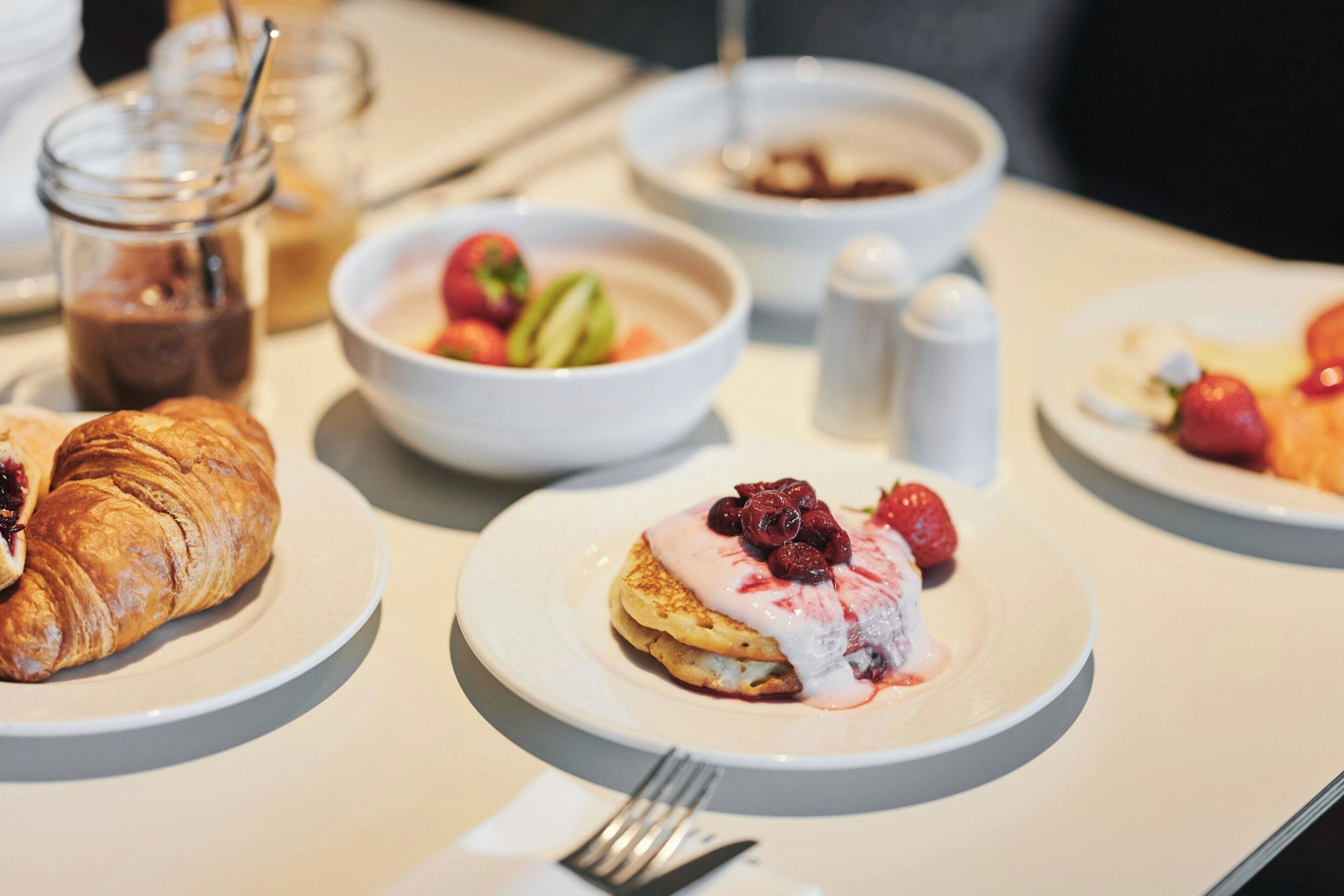 Ein Frühstückstisch mit Croissants, einer Obstschale und Pfannkuchen mit Beeren.