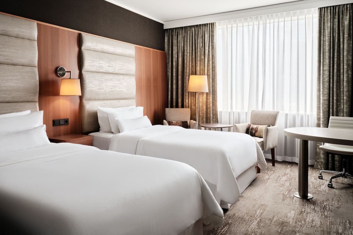 Ein Hotelzimmer mit zwei Betten, einem kleinen Tisch, einem Stuhl und einer Lampe.