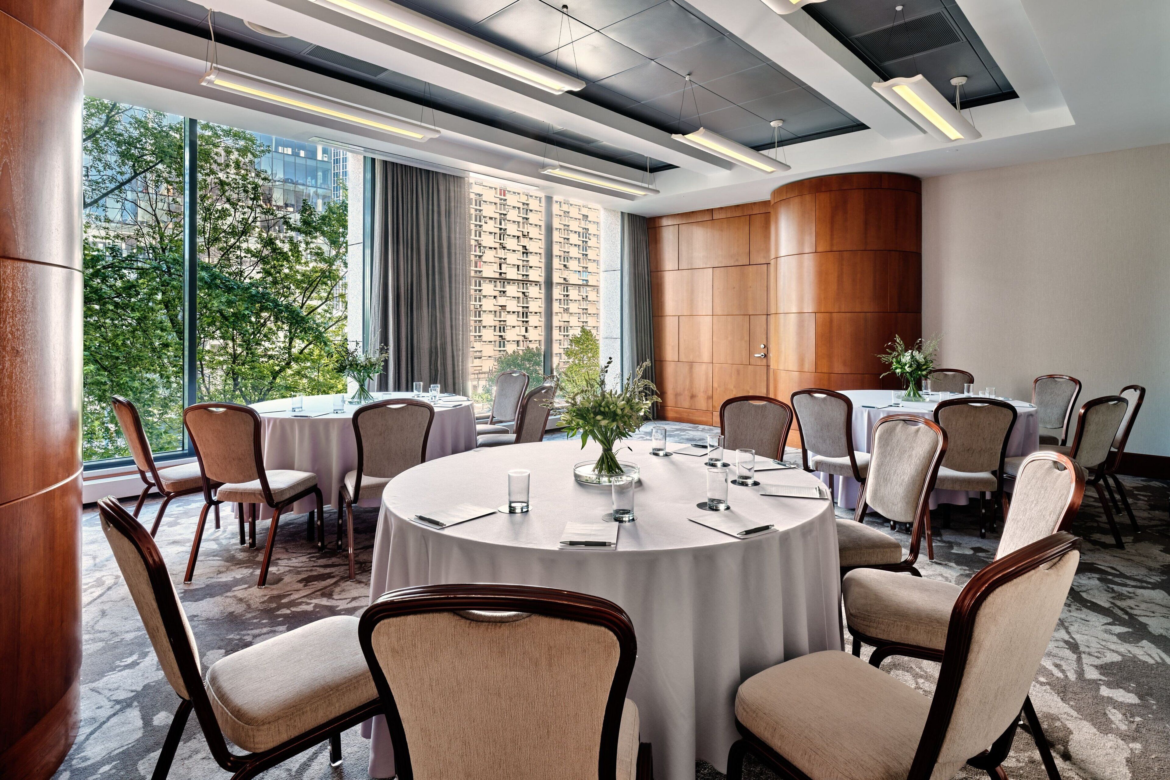 A conference room with round tables, chairs, and a large window with a city view.