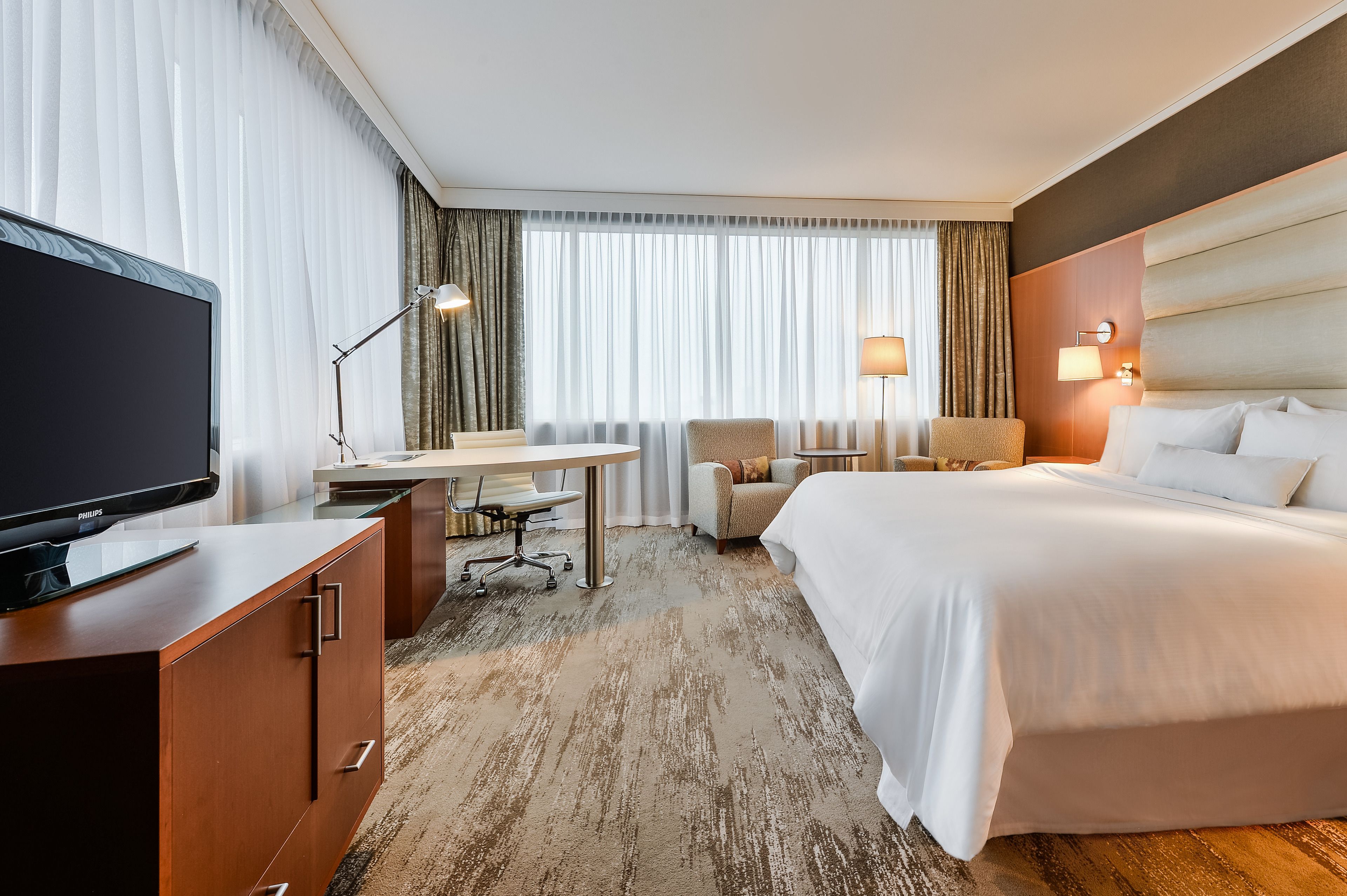 Una habitación de hotel con una cama grande, un escritorio con una silla, un televisor y una ventana con cortinas.