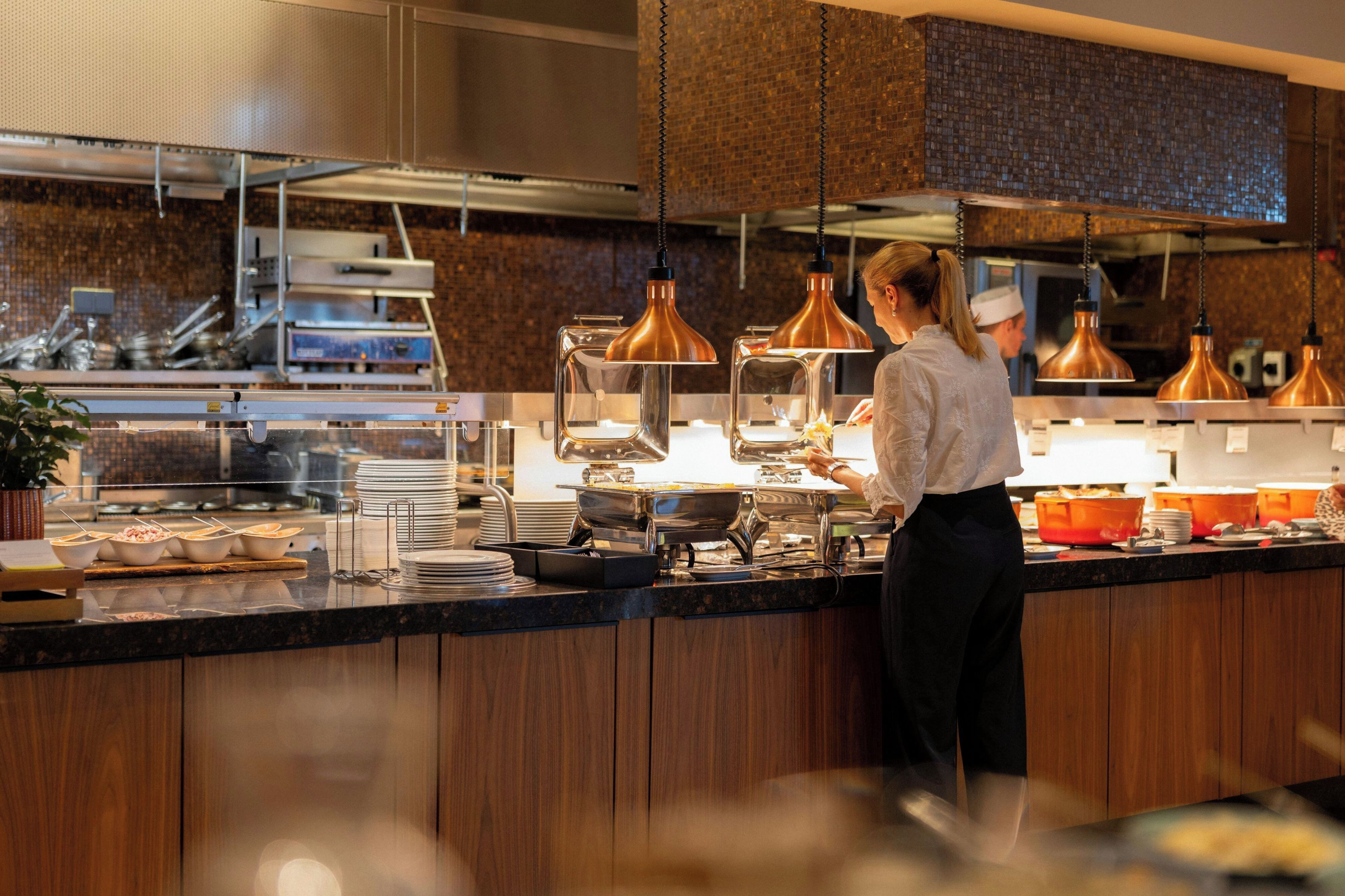 A kitchen with stainless steel appliances, copper pendant lights, and a buffet setup.