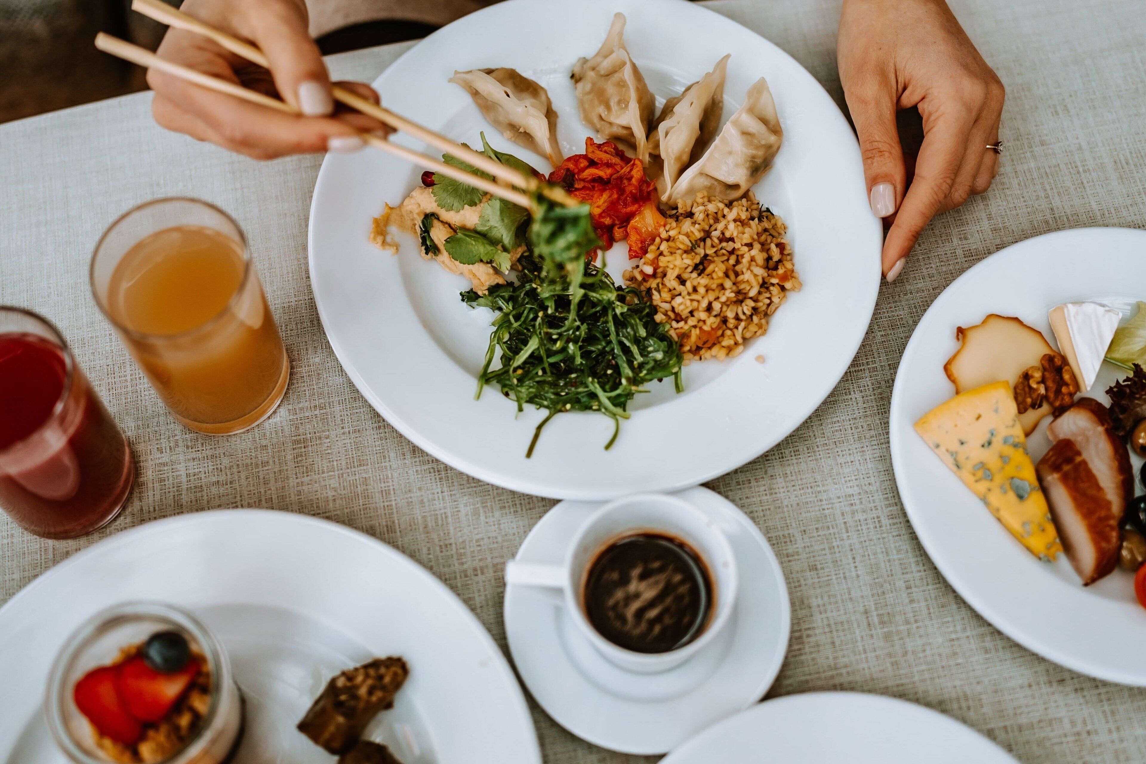 A table with plates of food, including dumplings, greens, and cheese, and a cup of coffee.