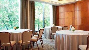 Un salón de conferencias con mesas redondas, sillas y ventanas grandes con cortinas.