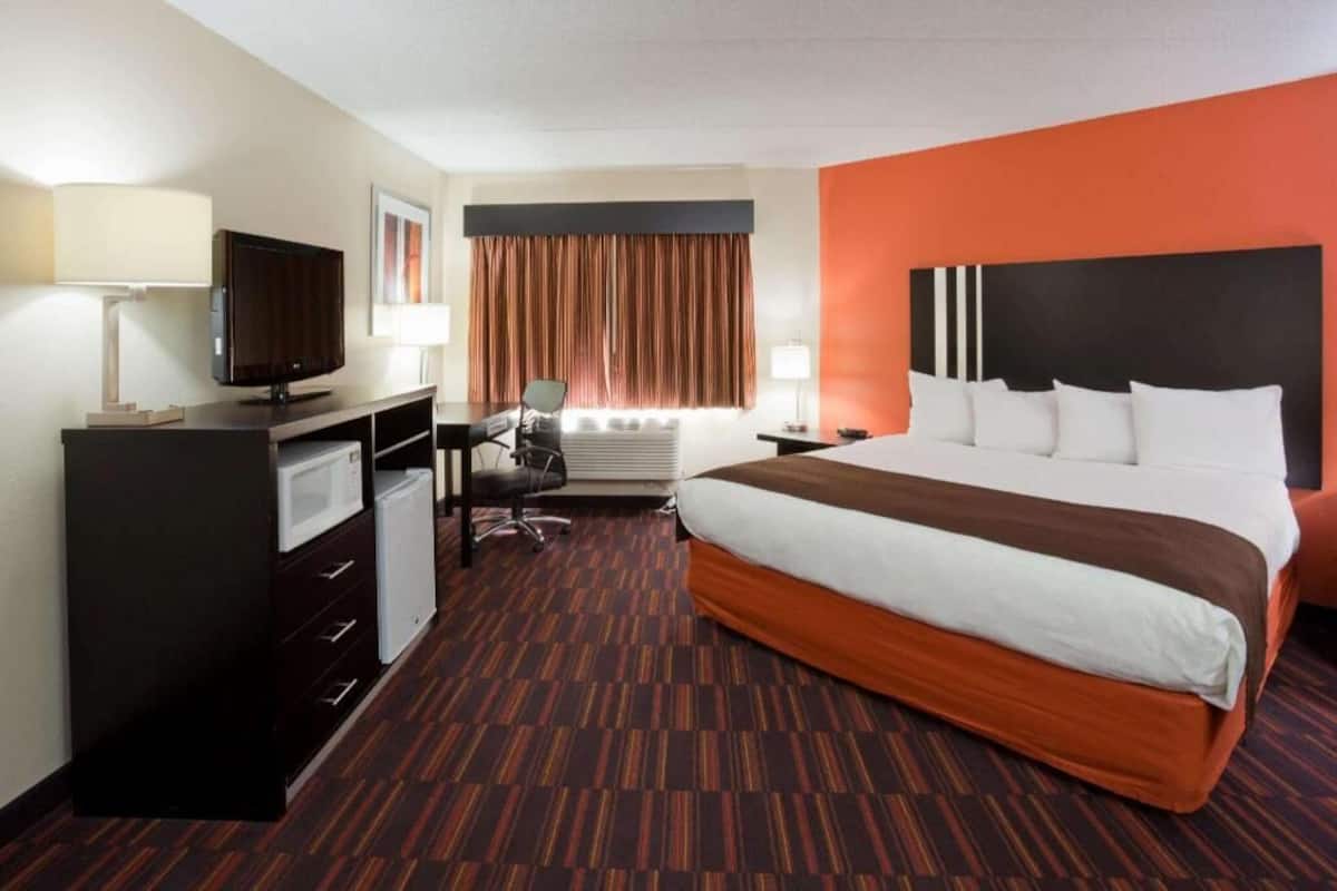 A hotel room with a large bed, a desk with a chair, a television, and a minibar.