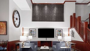 A modern lobby with a large wall-mounted TV, two sofas, a coffee table, and a staircase. - AmericInn by Wyndham Shakopee Near Canterbury Park (Shakopee)