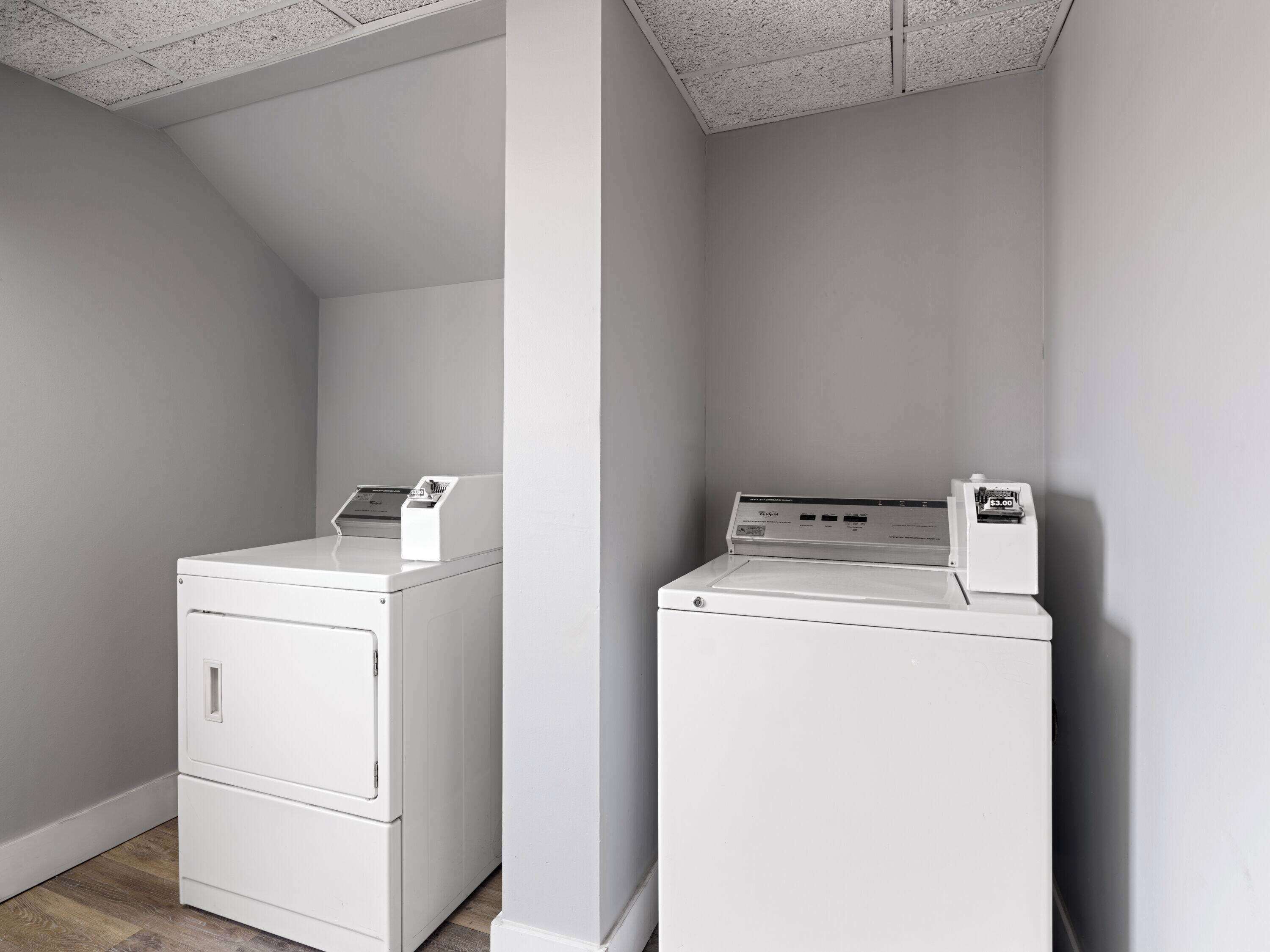 A laundry room with two white washers and dryers, a wooden floor, and a sloped ceiling.