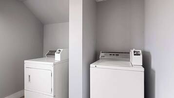 A laundry room with two white washers and dryers, a wooden floor, and a sloped ceiling.