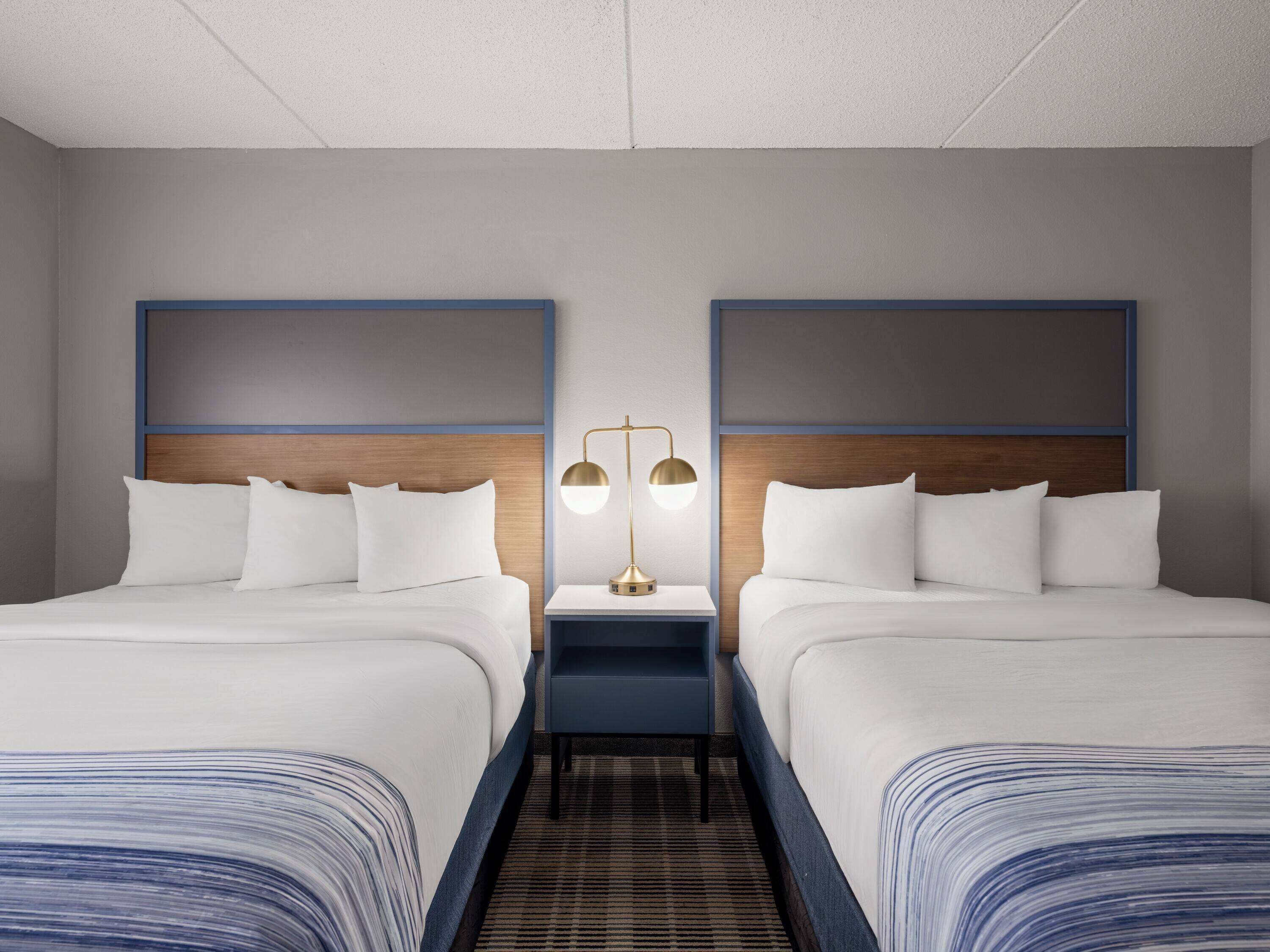 A hotel room with two beds, a nightstand, and a lamp.