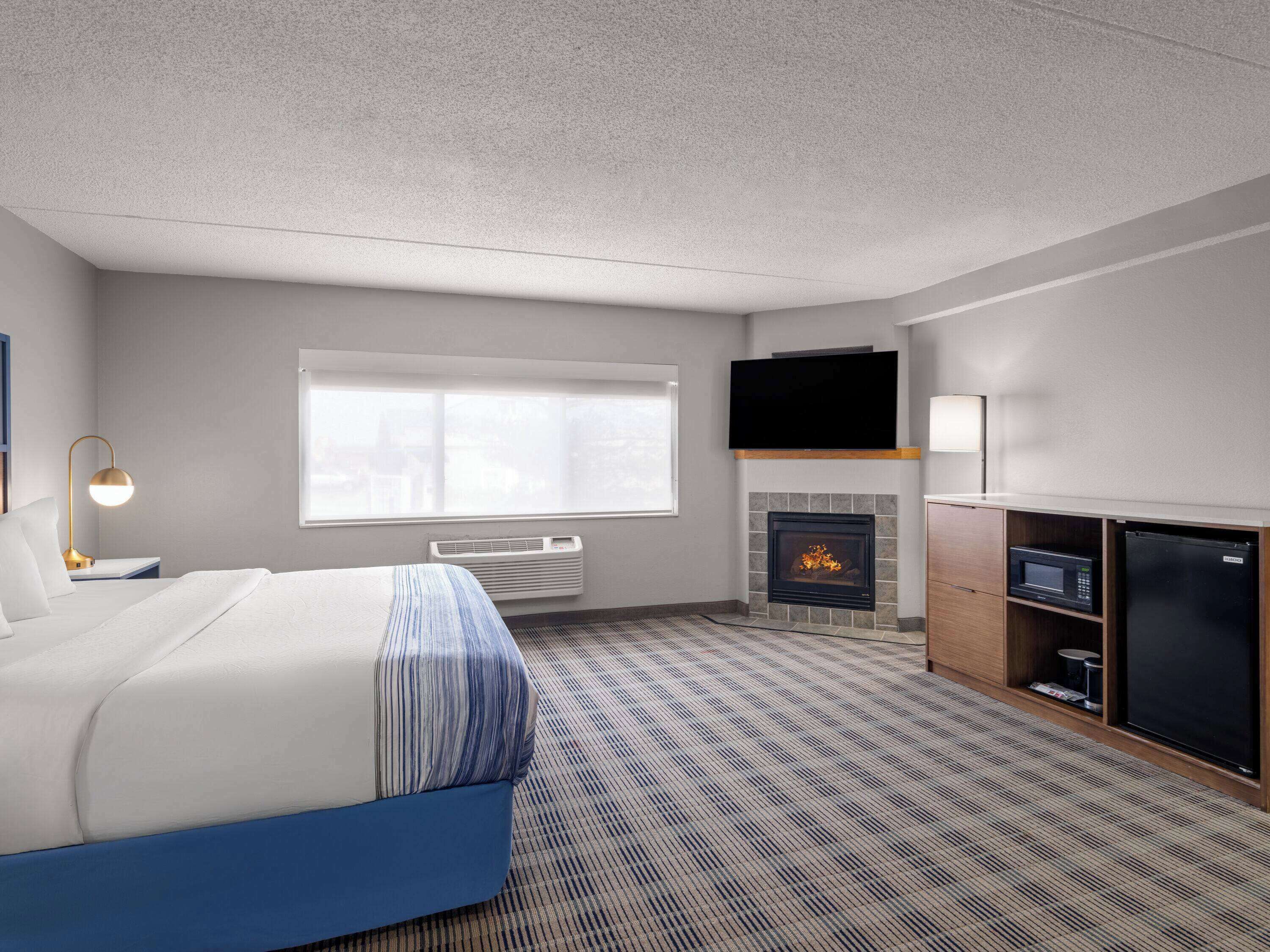 A hotel room with a bed, a flat-screen TV mounted above a fireplace, a microwave, and a refrigerator.
