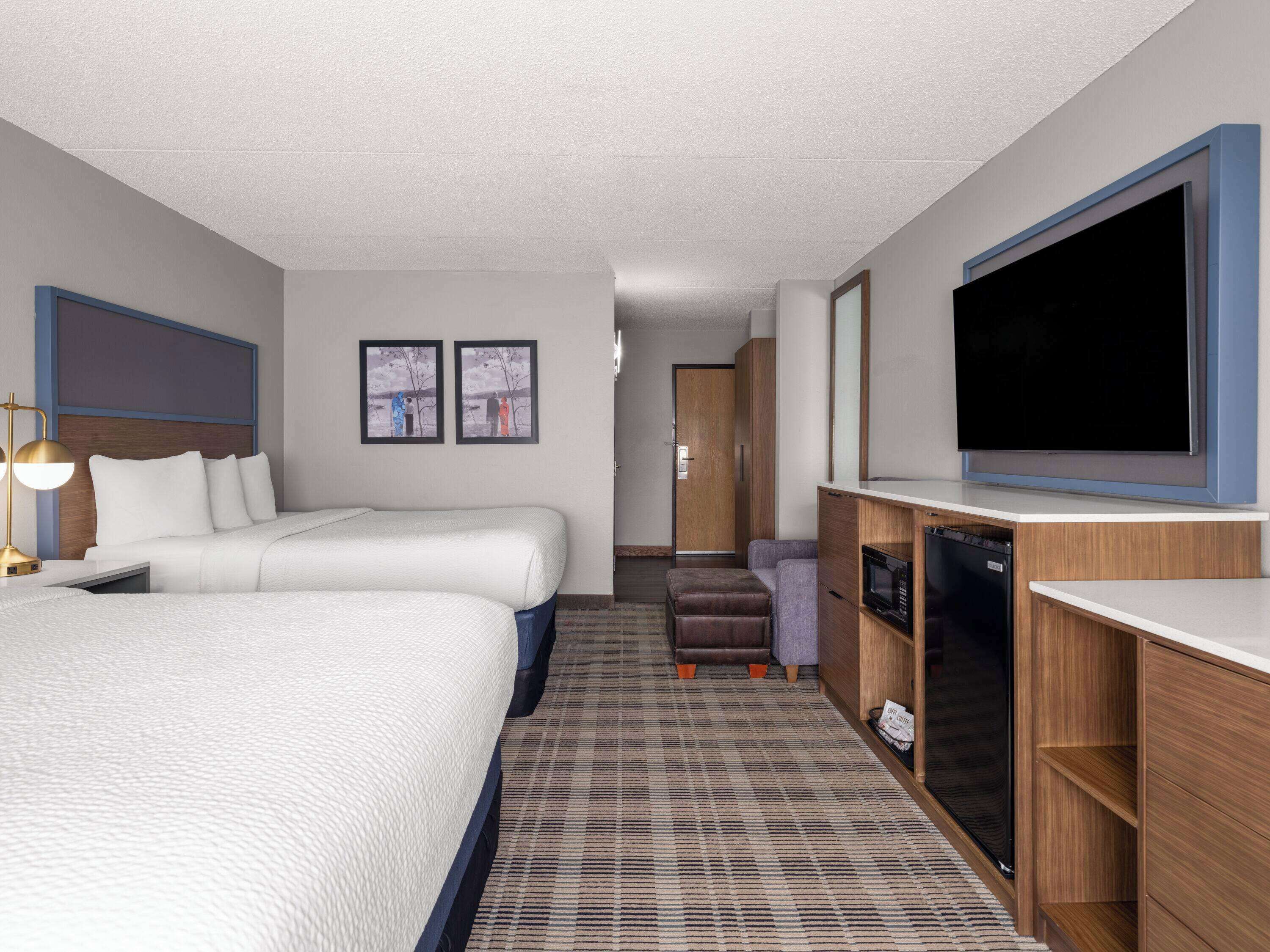 A hotel room with two beds, a desk with a TV, a microwave, and a wardrobe.