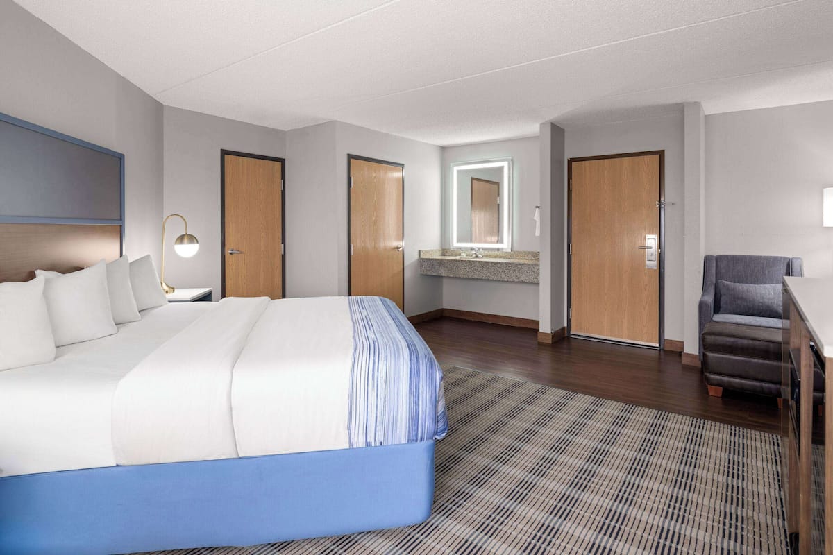 A hotel room with a large bed, a desk with a chair, a bathroom with a mirror, and two doors.