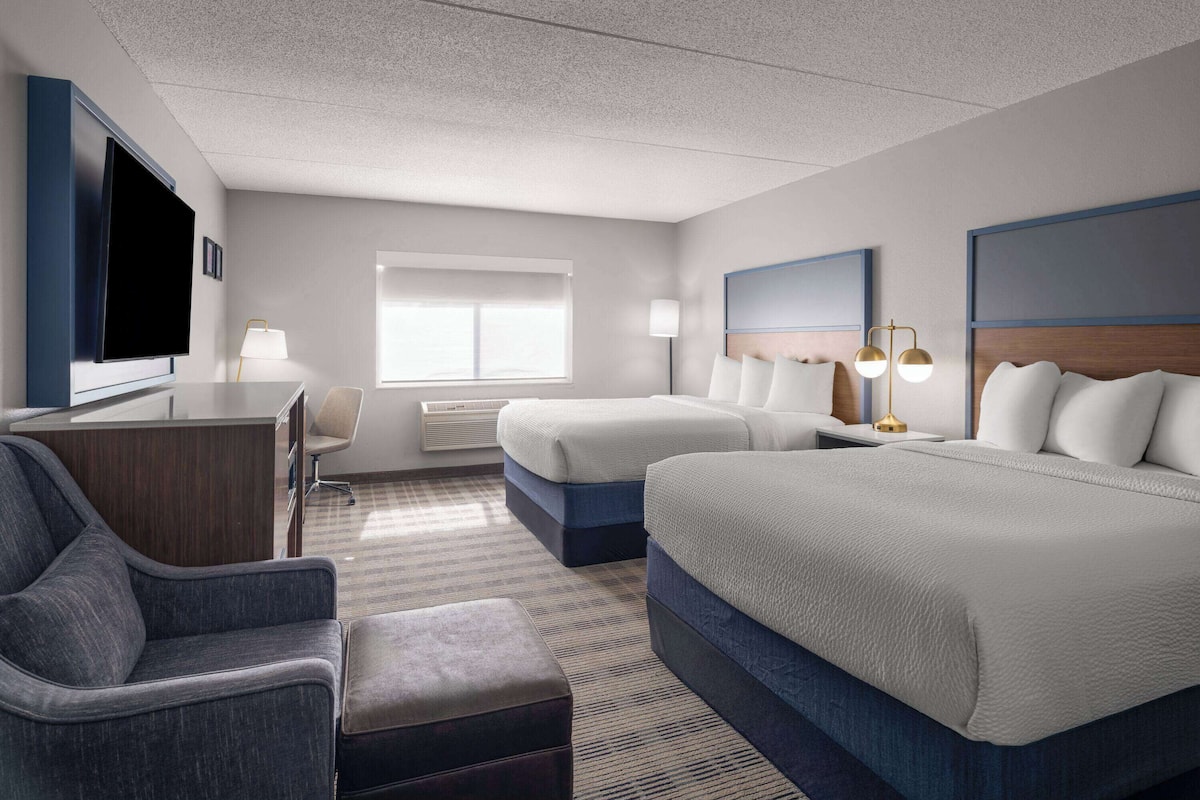 A hotel room with two beds, a desk, a chair, a TV, and a window.