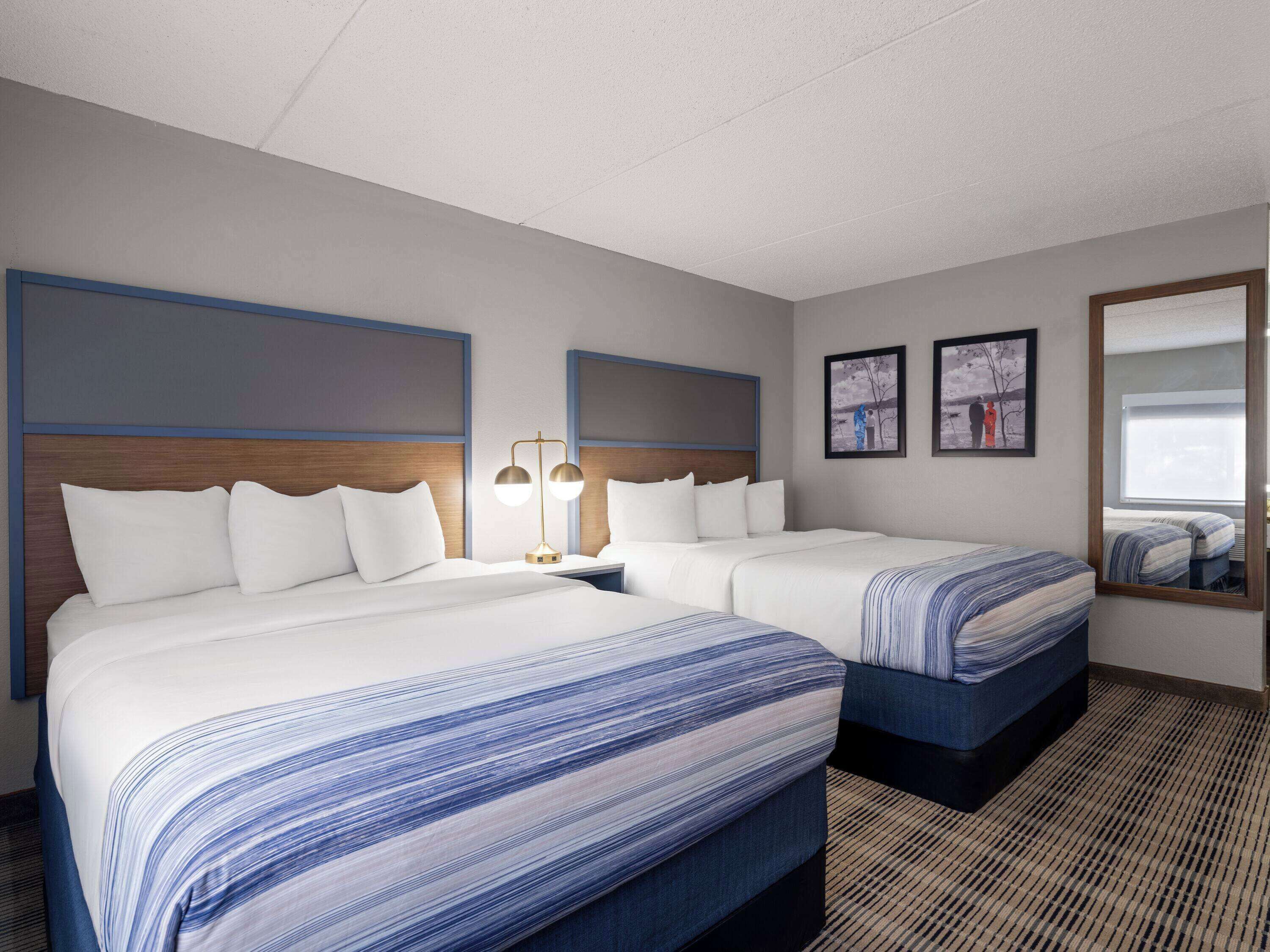 A hotel room with two beds, a large mirror, and artwork on the walls.
