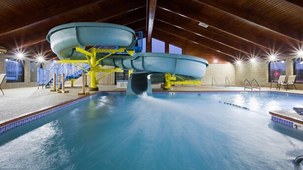 An indoor swimming pool with a water slide, wooden ceiling, and tiled walls. - AmericInn by Wyndham Shakopee Near Canterbury Park (Shakopee)