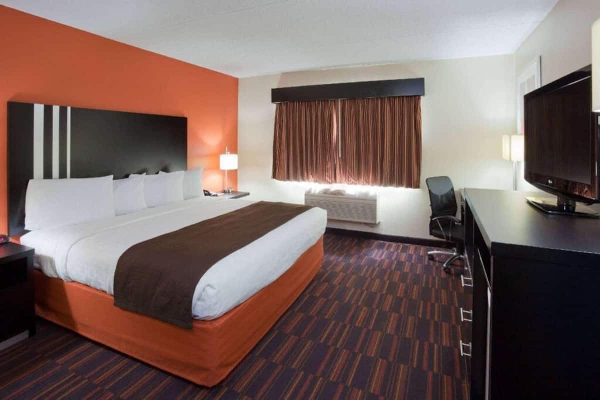 A hotel room with a large bed, a desk with a television, a chair, a lamp, and a window with curtains.